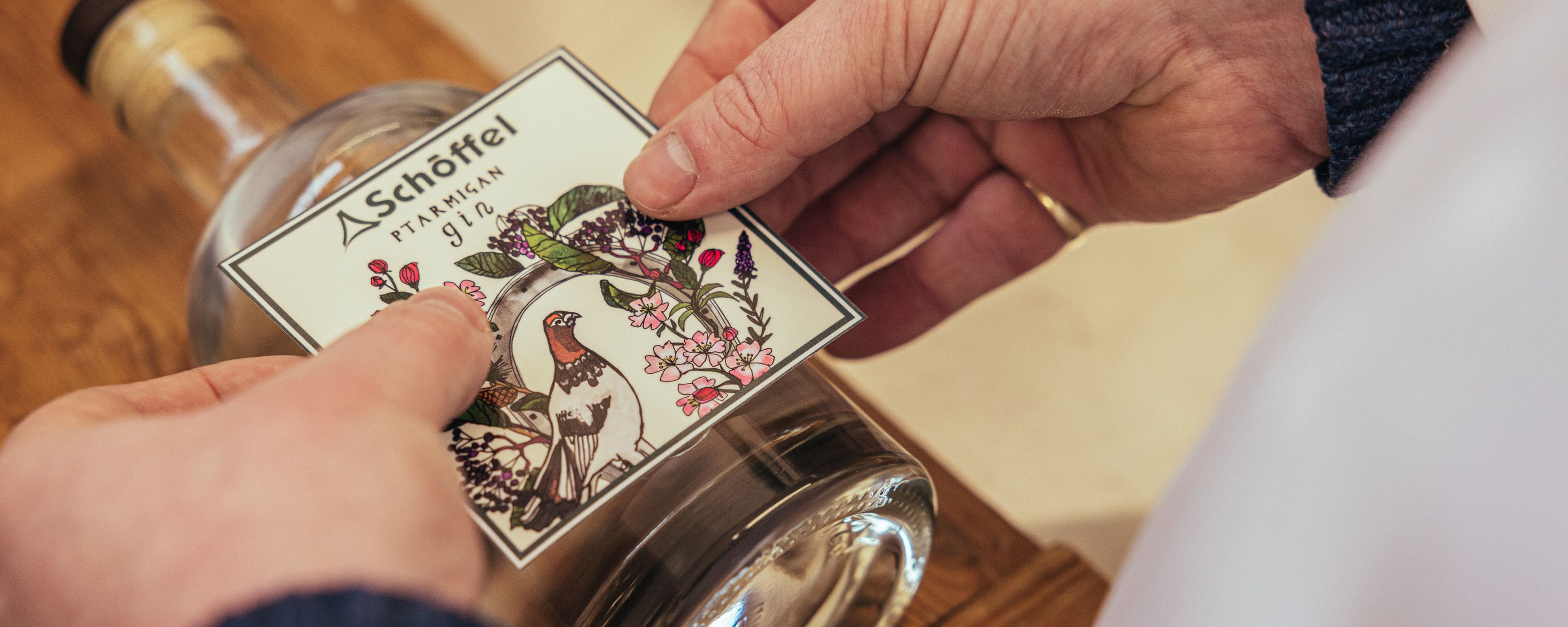 A close up of a gin bottle with the label being applied to the front.