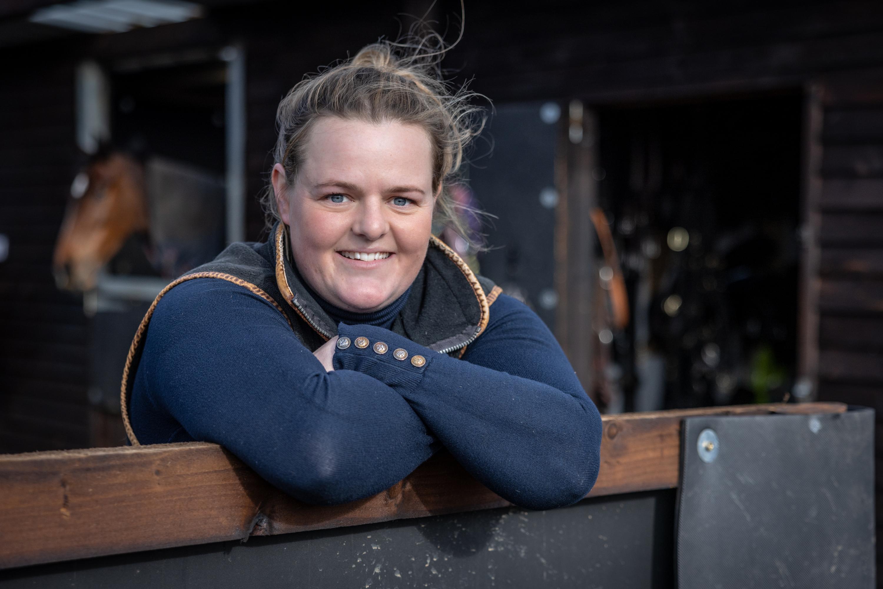 A woman is seen leaning on a gate looking forward and smiling.