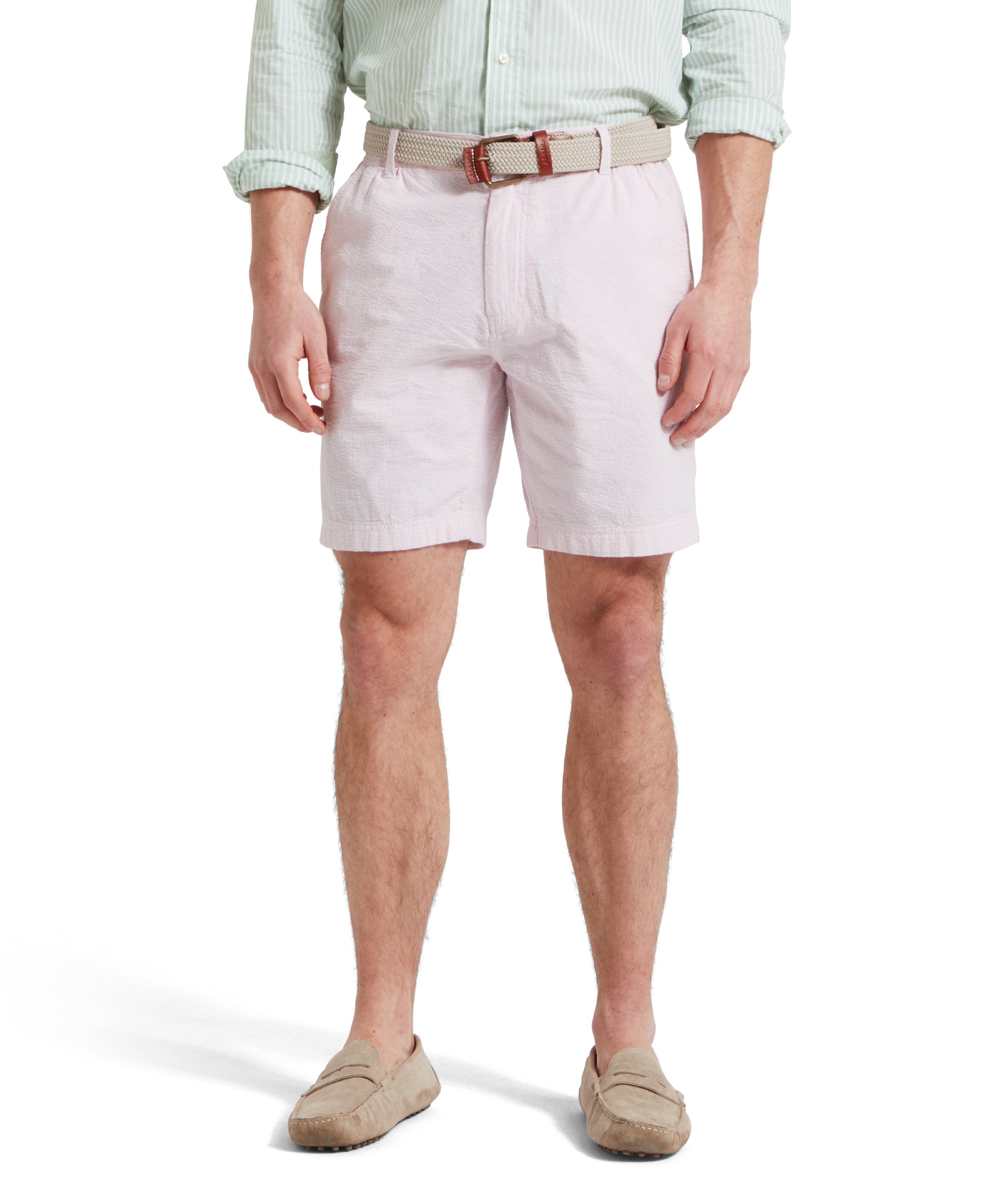 A close up of a male model wearing a light pink shorts with a tucked in light green and white striped shirt. It is paired with a beige woven belt and tan loafers.