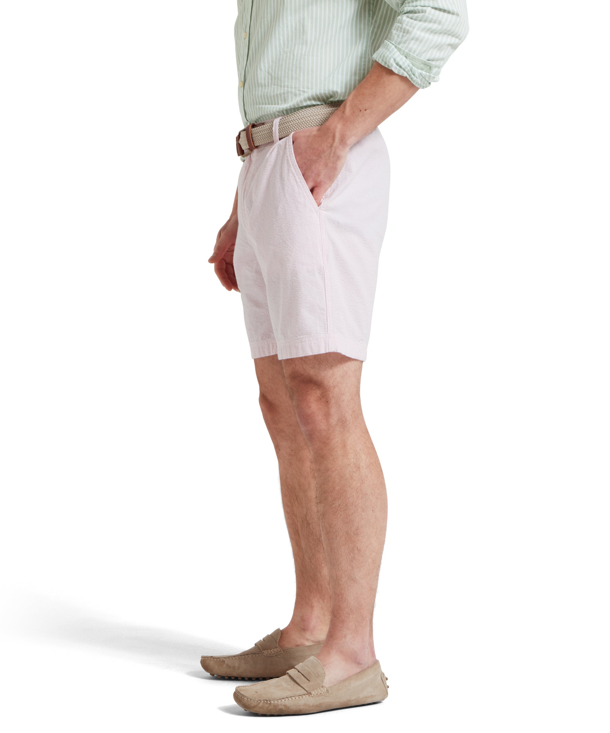 A side image of a male model wearing a light pink shorts with a tucked in light green and white striped shirt. It is paired with a beige woven belt and tan loafers. He is standing in a relaxed pose with one hand in his pocket.