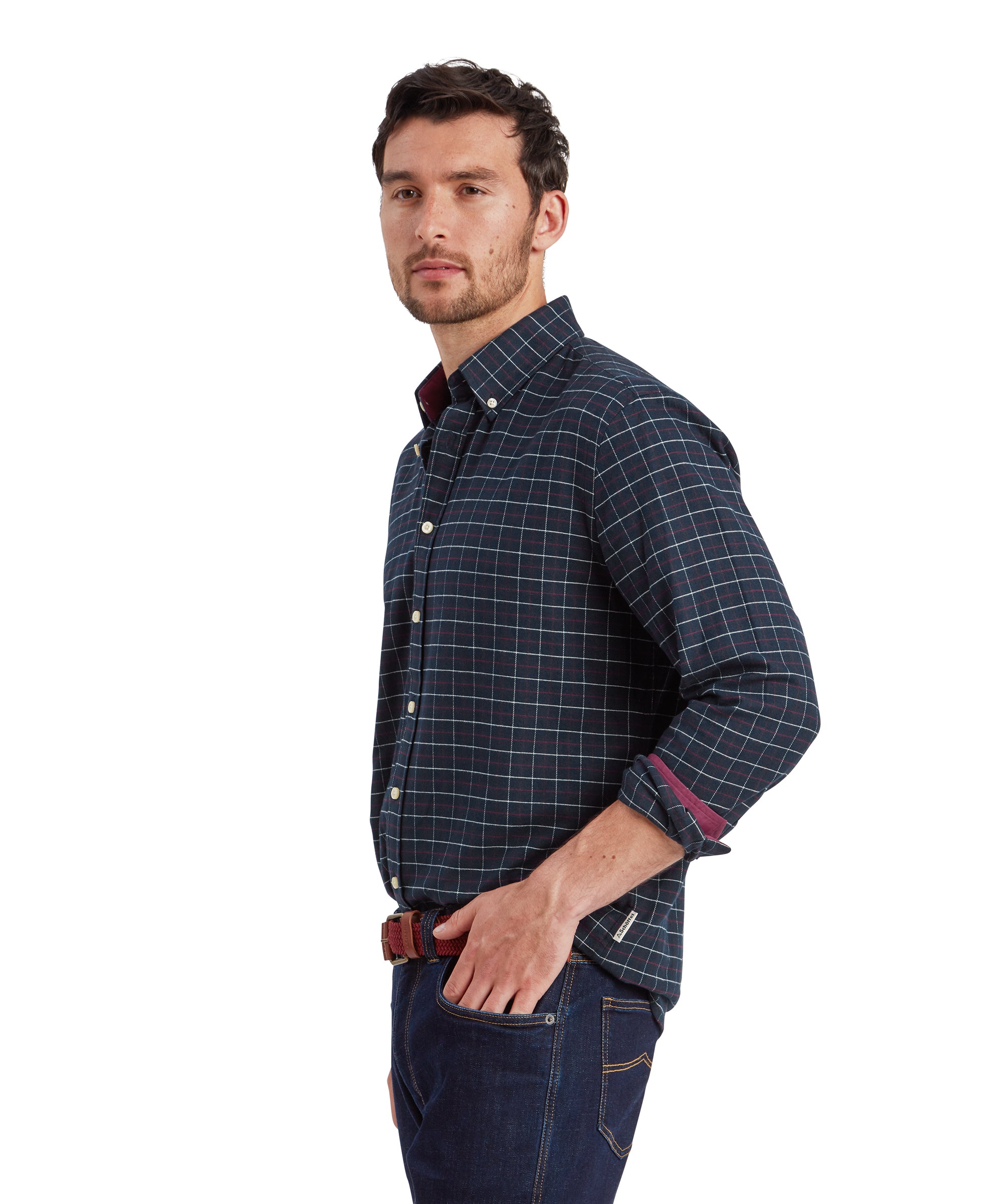 A side view of the male model showcasing the left side of the Schöffel Aldeburgh Tailored Shirt for Men in Navy. The model has his left hand casually placed in his jean pocket, highlighting the rolled-up sleeves that reveal a contrasting maroon inner lining. He gazes slightly past the camera.