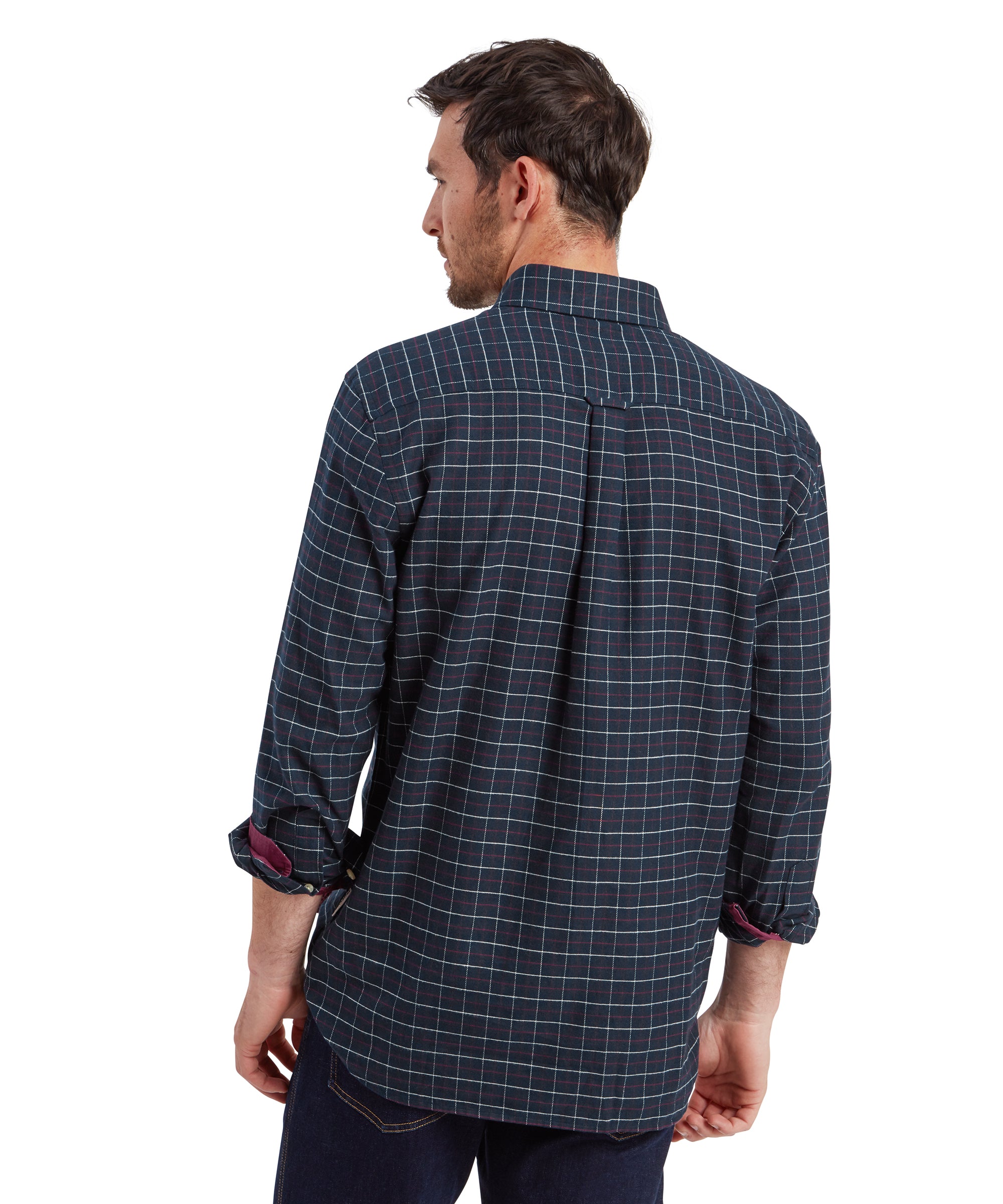 The back view of the male model, displaying the Schöffel Aldeburgh Tailored Shirt for Men in Navy's rear design. The shirt has a yoke with a box pleat at the back, providing a relaxed fit. The model’s sleeves are rolled up, revealing the contrasting maroon lining. The hem of the shirt is untucked.