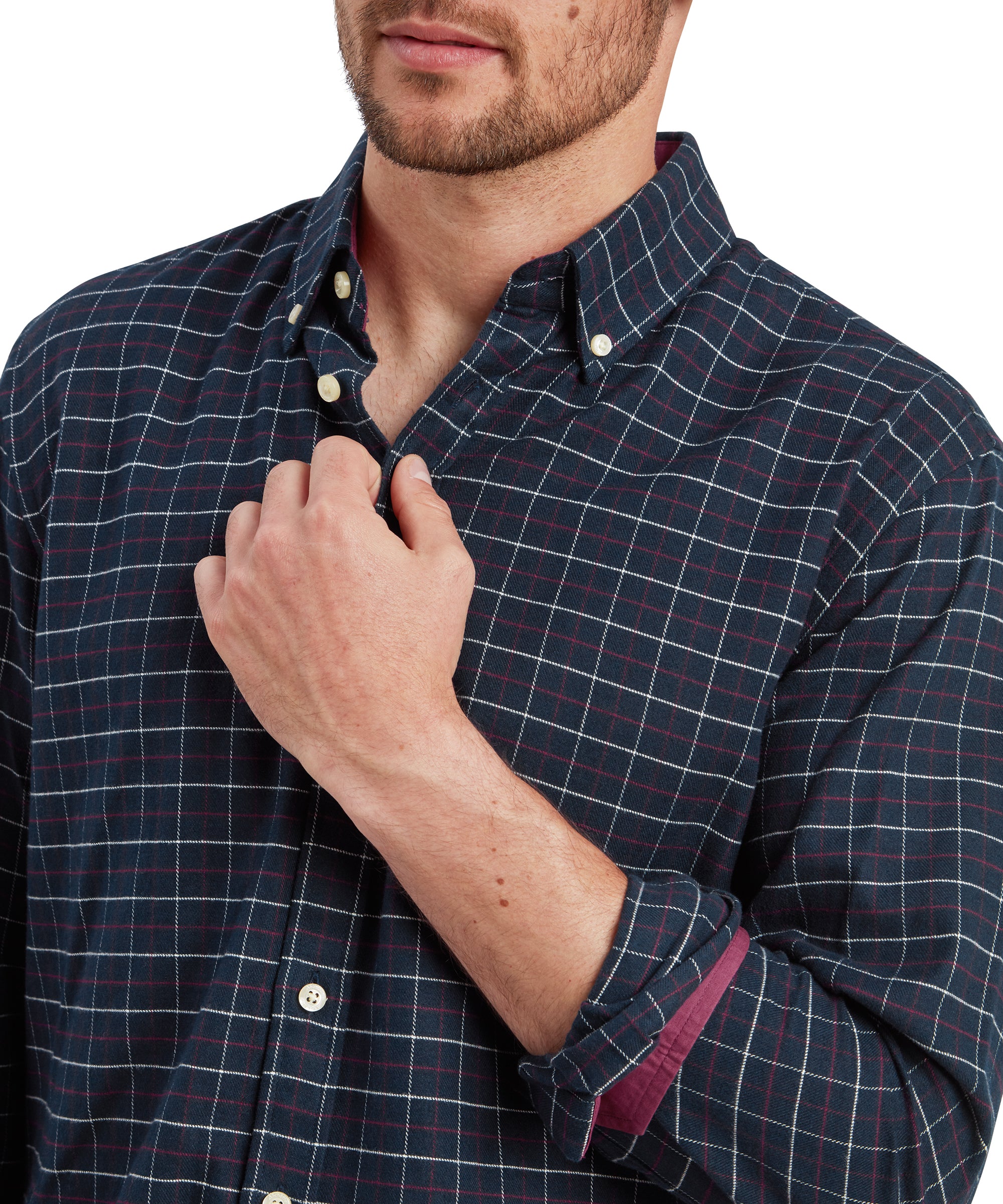 A close-up shot of the male model's chest, showcasing the button-down collar of the Schöffel Aldeburgh Tailored Shirt for Men in Navy. The model has his right hand holding the shirt's collar near the top button, which is unbuttoned. The checkered pattern features navy, green, and subtle red stripes.