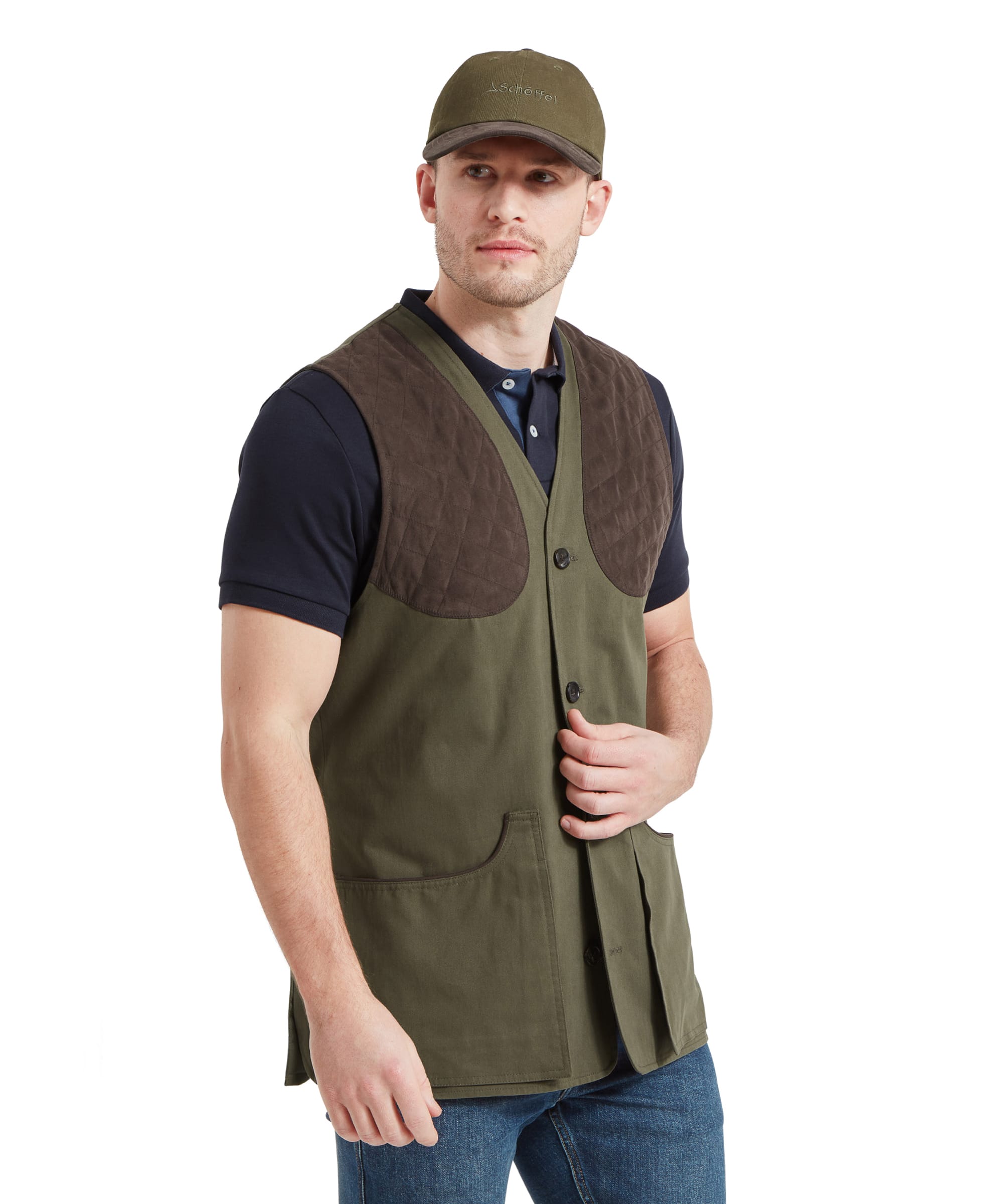 A man wearing a Schöffel All Season Shooting Vest for Men in Green with quilted shoulder pads, a navy blue shirt, and a matching green cap. He is looking to the side with one hand in his vest pocket.