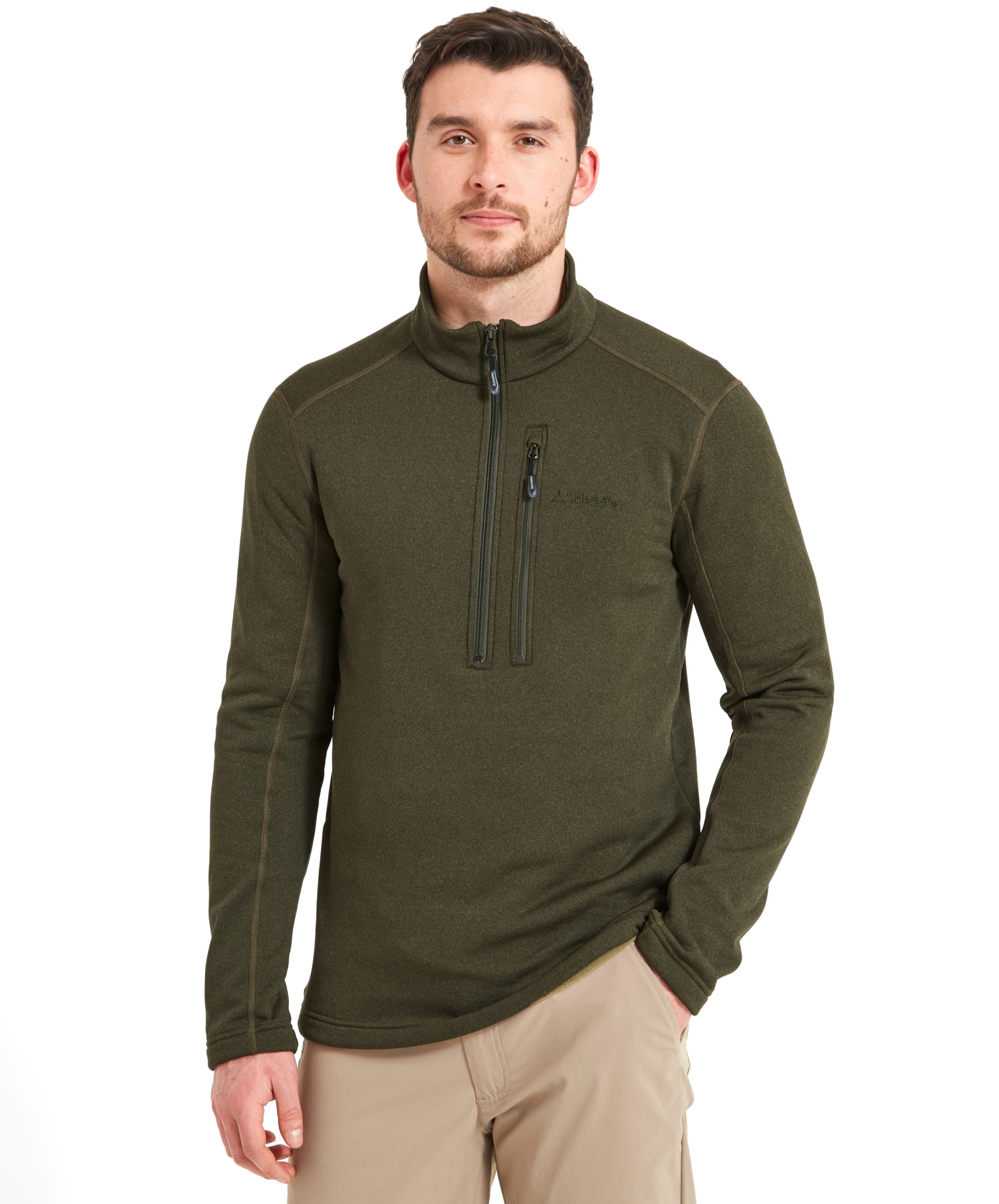 A man wearing a Schöffel Annan II Technical 1/4 Zip for Men in Green, standing with one hand in his pocket and looking straight ahead. He is also wearing beige trousers.