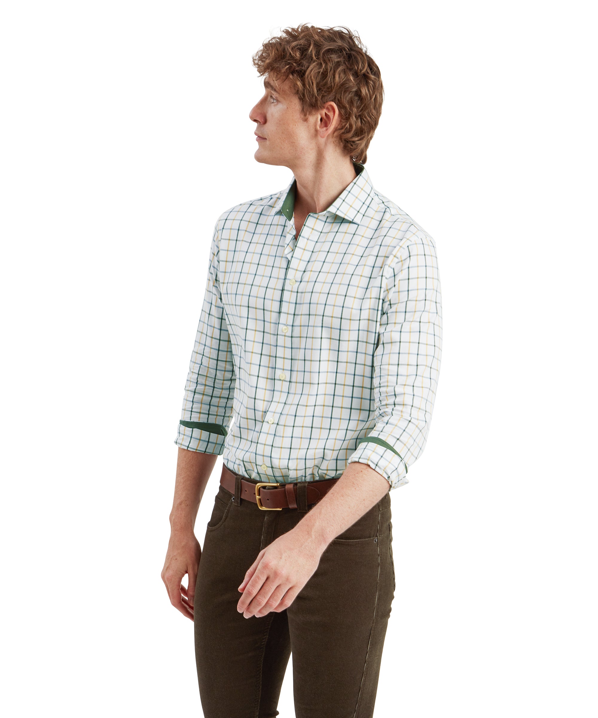 Side profile of the man wearing the same outfit. He is standing in a relaxed pose, looking off to his right. The shirt's tailored fit is visible, showing off its clean lines and well-fitted structure. The contrast between the Schöffel Baconsthorpe Tailored Shirt for Men in Green’s light color and the dark pants is prominent in this angle.