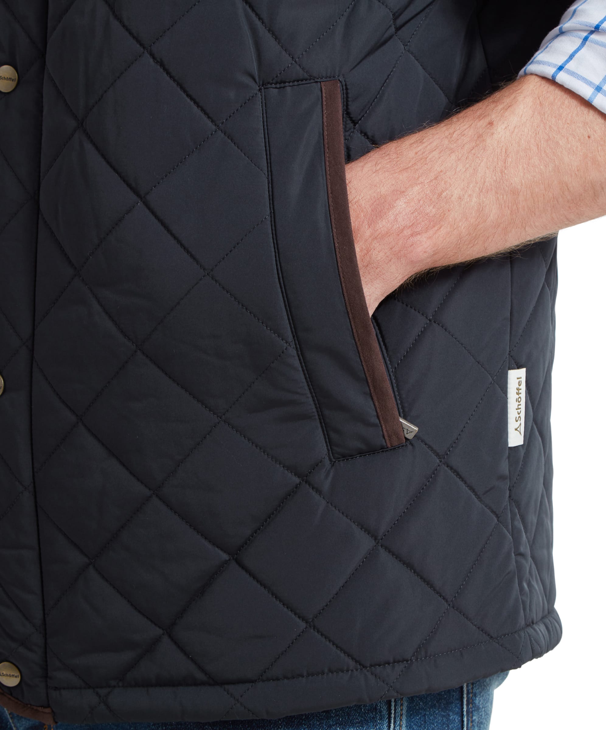 A close-up shot of a man wearing a Schöffel Barrowden Quilt Gilet for Men in Blue with brown trim, showing his hand in the front pocket and the "Schöffel" logo tag near the pocket.