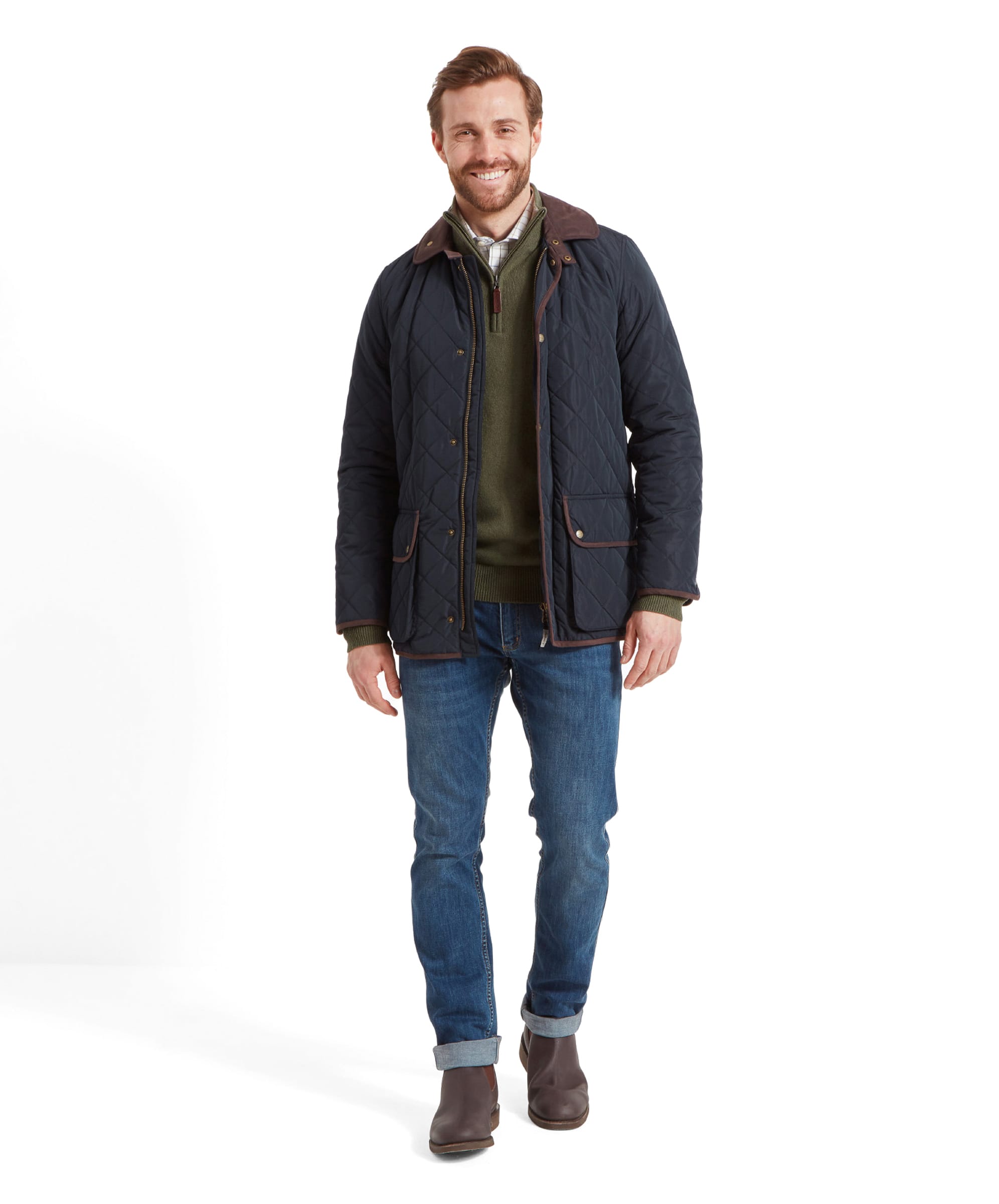 Full-body view of the man in the Schöffel Barrowden Quilt Jacket for Men in Blue, green sweater, and blue jeans, standing and smiling.