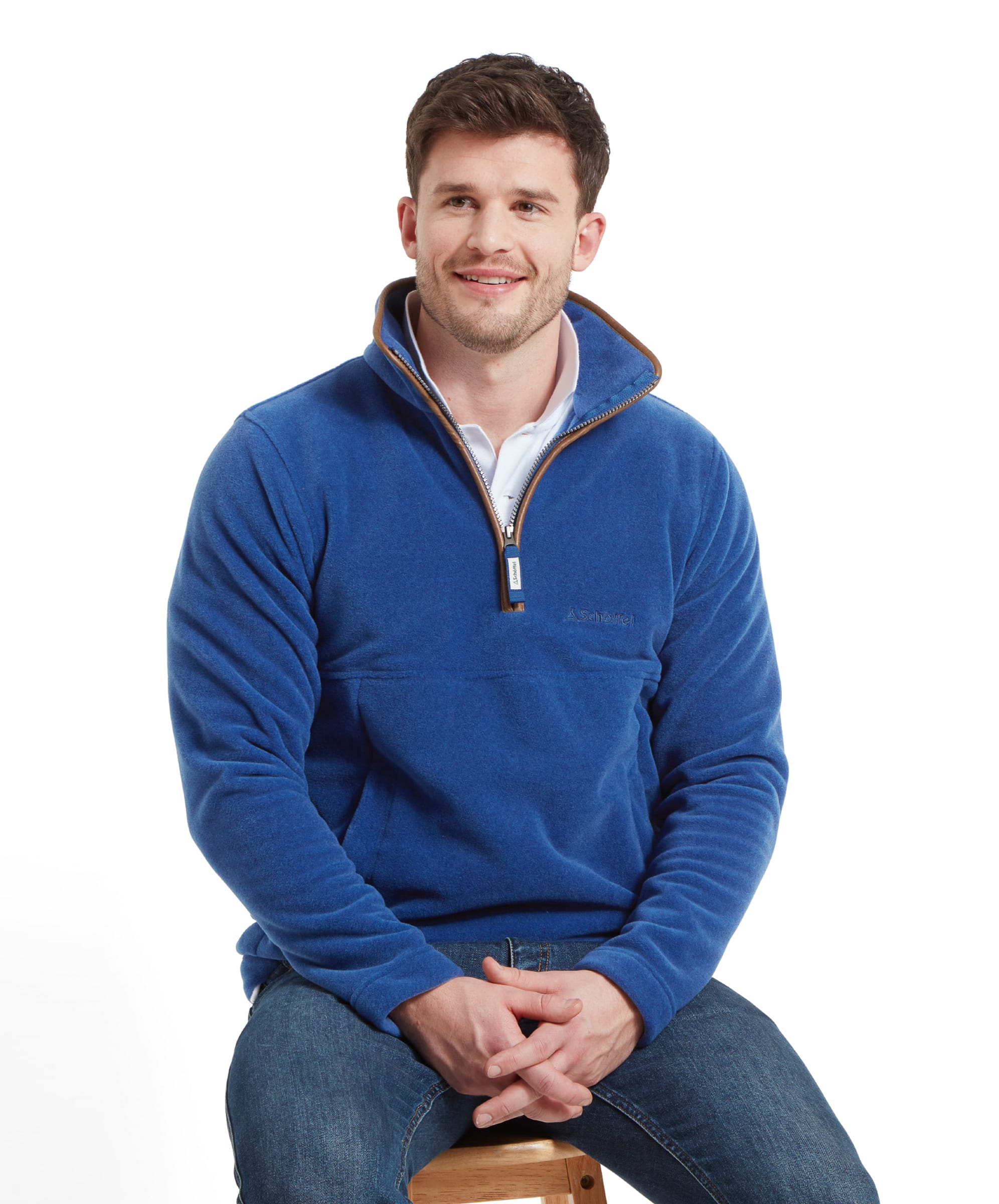 The man sitting on the stool, facing the camera and smiling, with both hands resting on his lap whilst wearing the Schöffel Berkeley Fleece 1/4 Zip Fleece for Men in Blue