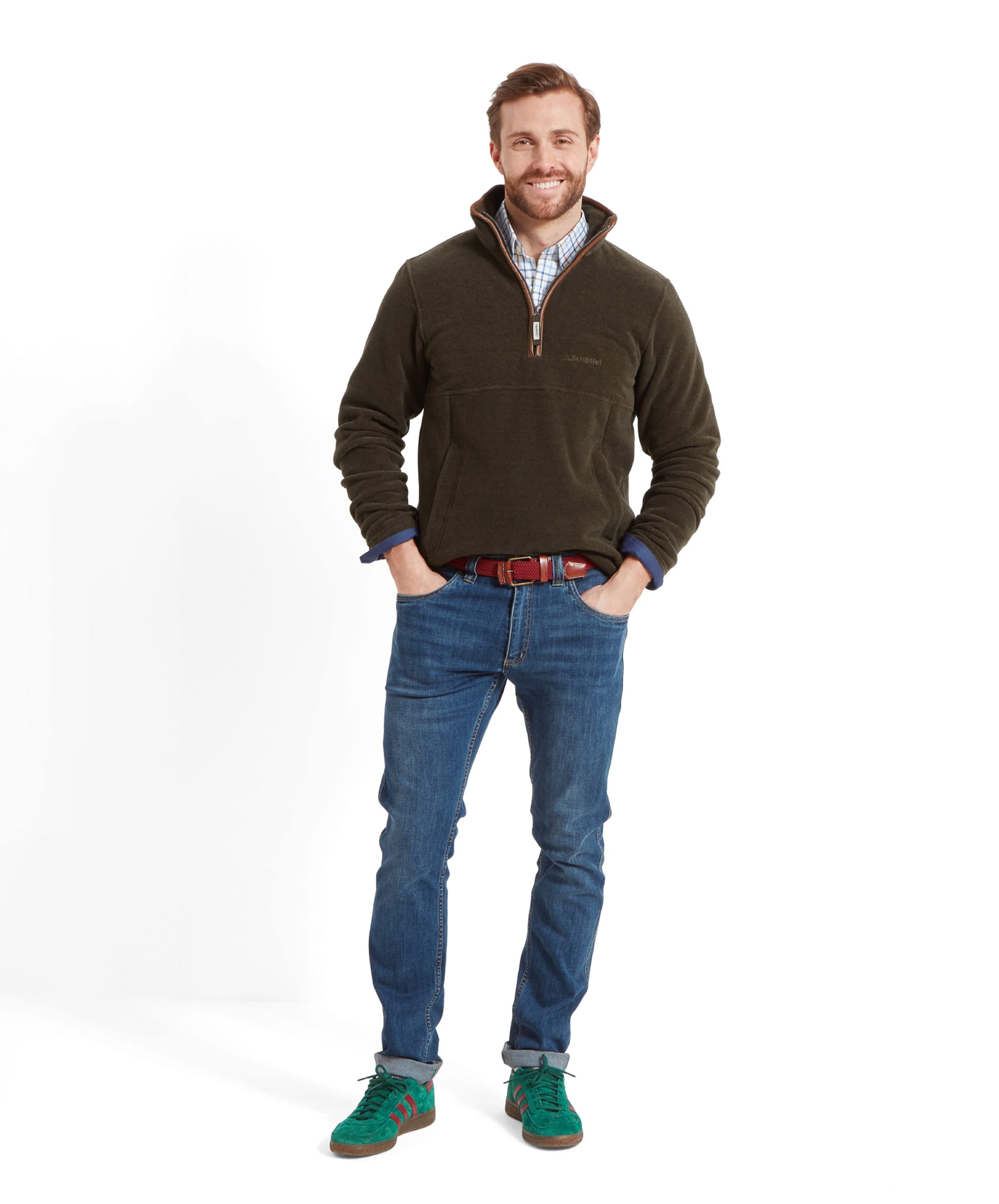 Full-body view of man in Schöffel Berkeley Fleece 1/4 Zip Fleece for Men in Olive Green, wearing light blue jeans, green trainers, a checked shirt and a brown belt, standing with hands in pockets looking forward and smiling.