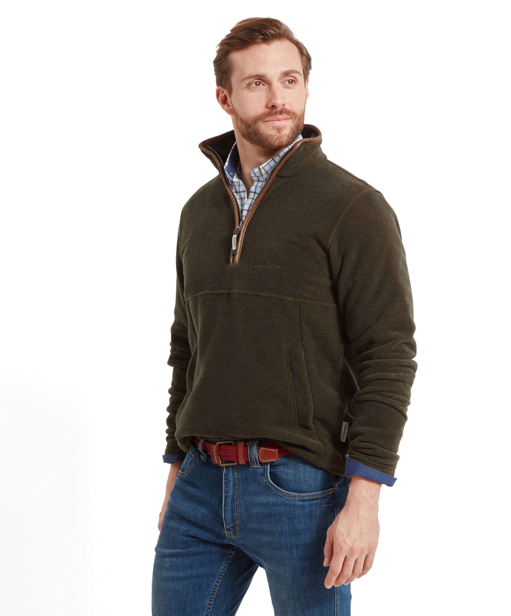 Man in Schöffel Berkeley Fleece 1/4 Zip Fleece for Men in Olive Green, wearing light blue jeans, a checked shirt and a brown belt, standing with his frame to the side, looking away.