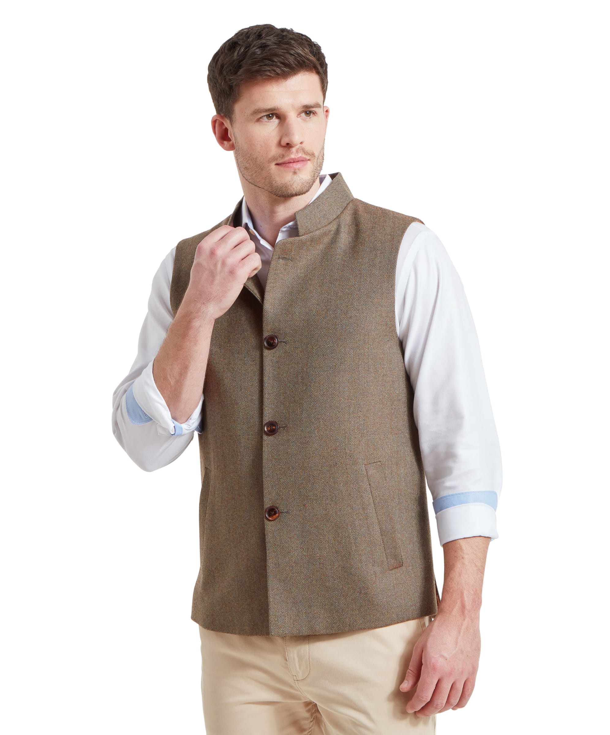 A man wearing a Schöffel Berwick Nehru Tweed Waistcoat for Men in Green over a white shirt with rolled-up sleeves. He is standing, looking to the right, and holding the lapel of his waistcoat.