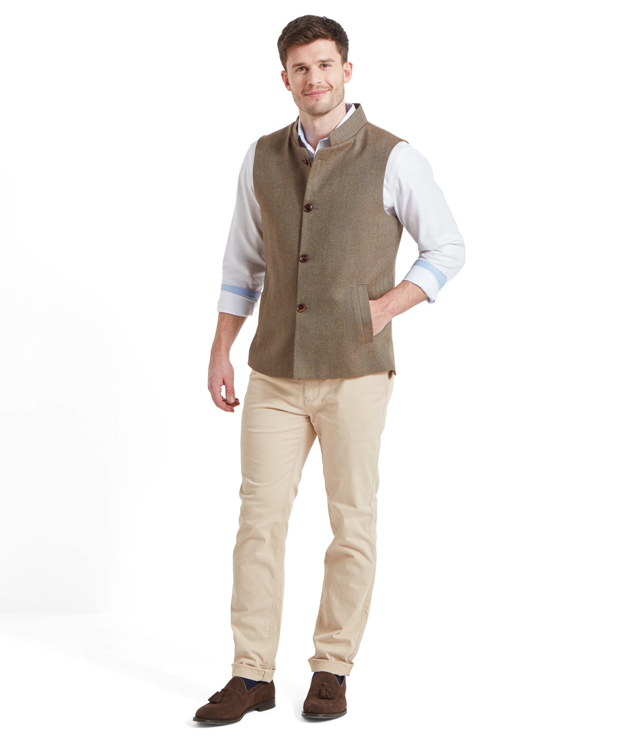 A full-body view of a man wearing a Schöffel Berwick Nehru Tweed Waistcoat for Men in Green over a white shirt with rolled-up sleeves, beige trousers, and brown shoes, standing and smiling.