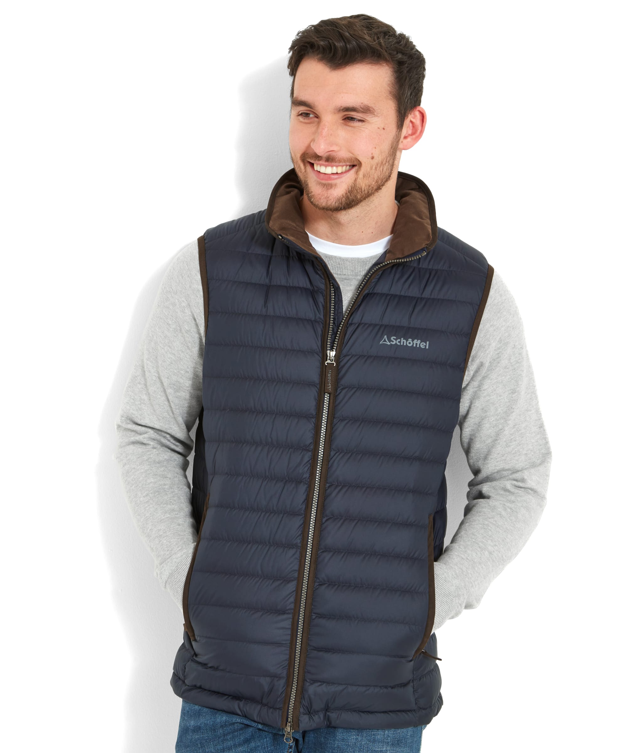 A man wearing a Schöffel Bowden Down Gilet for Men in Blue over a grey long-sleeve shirt, smiling while looking slightly to the side.