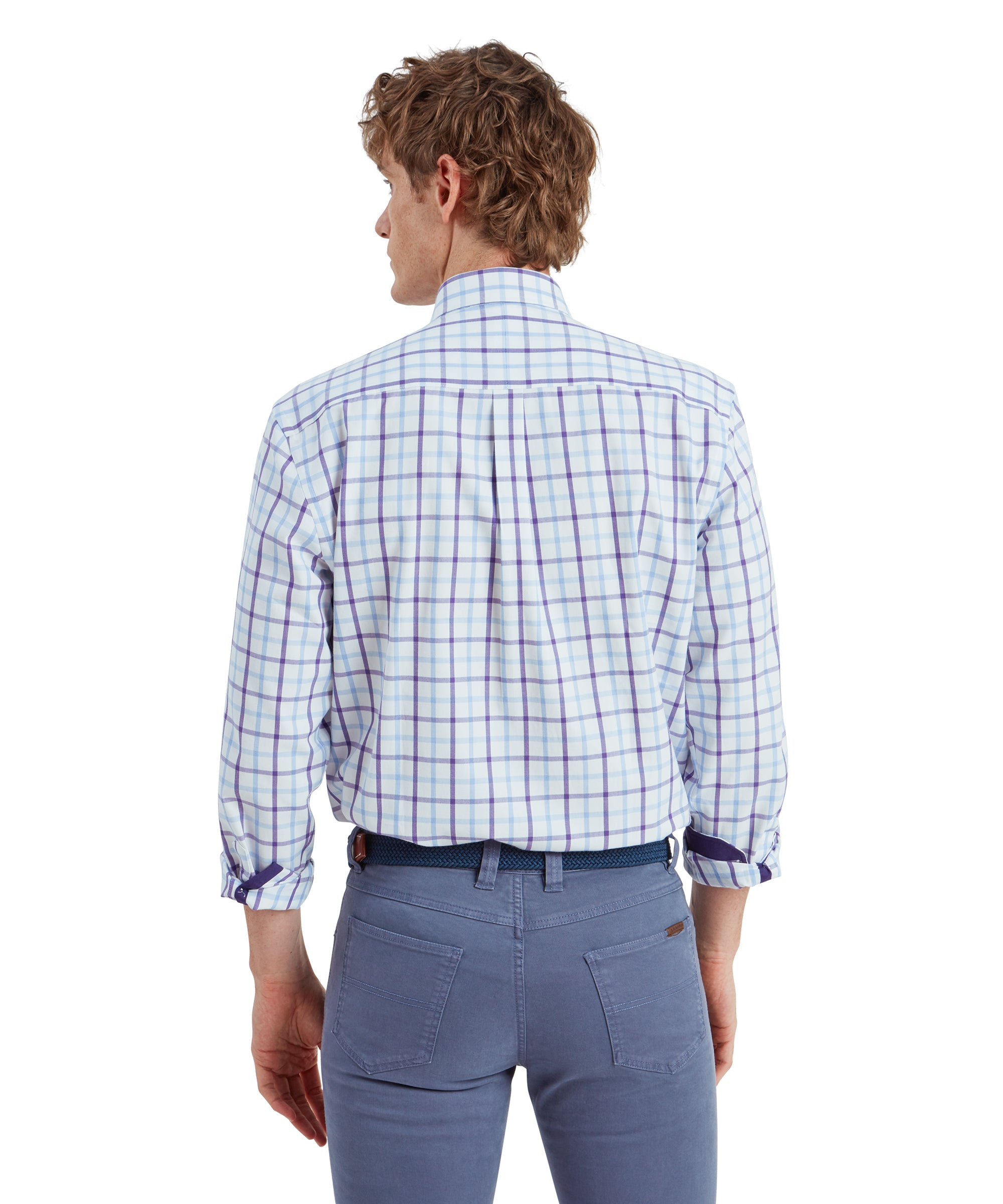 A rear view of the young man wearing the Schöffel Brancaster Classic Shirt for Men in Purple. The shirt fits snugly, showing the man’s back and shoulders clearly. The shirt is tucked into slim-fit light blue pants, emphasising a clean and neat look. The blue woven belt is also visible from the back.