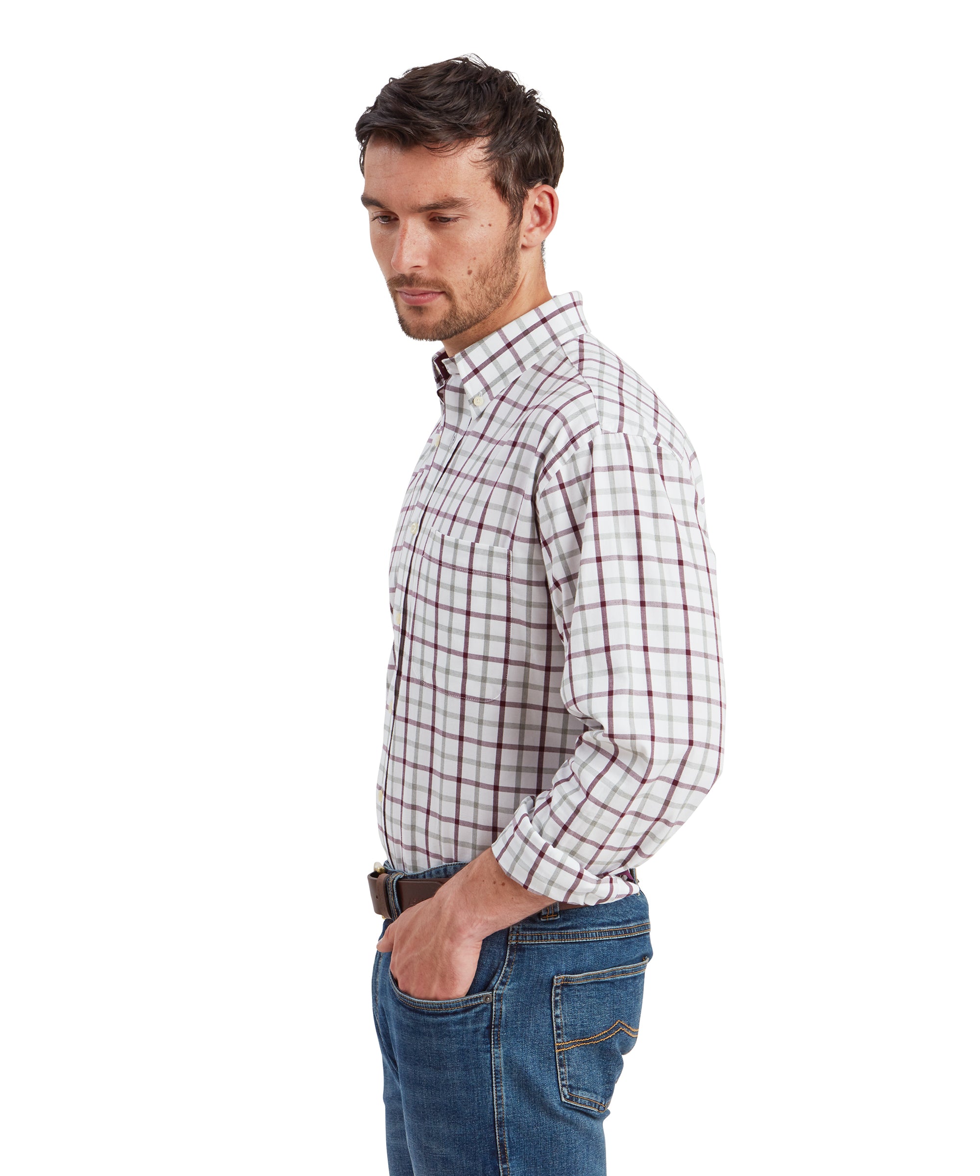 A side profile of the man wearing the same outfit, focusing on the shirt's fit along the shoulders and sleeves. The collar of the Schöffel Brancaster Classic Shirt for Men in Red is clearly visible, and the rolled-up sleeves reveal a bit of the inner lining. The man is standing with one hand in his pocket, looking downward with a thoughtful expression.