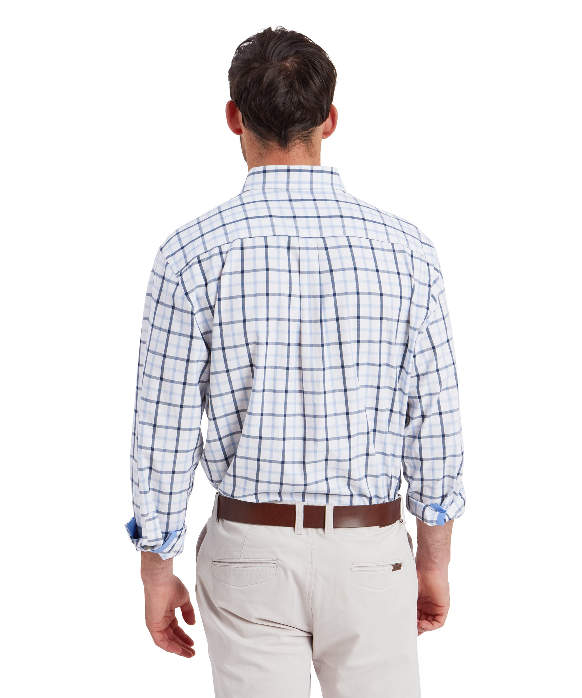 A rear view of the man displays the back of the Schöffel Brancaster Classic Shirt for Men in Dark Blue, revealing its relaxed fit with a single pleat near the shoulders for extra comfort. The light beige chinos complement the shirt, and the brown leather belt adds a cohesive touch to the look.