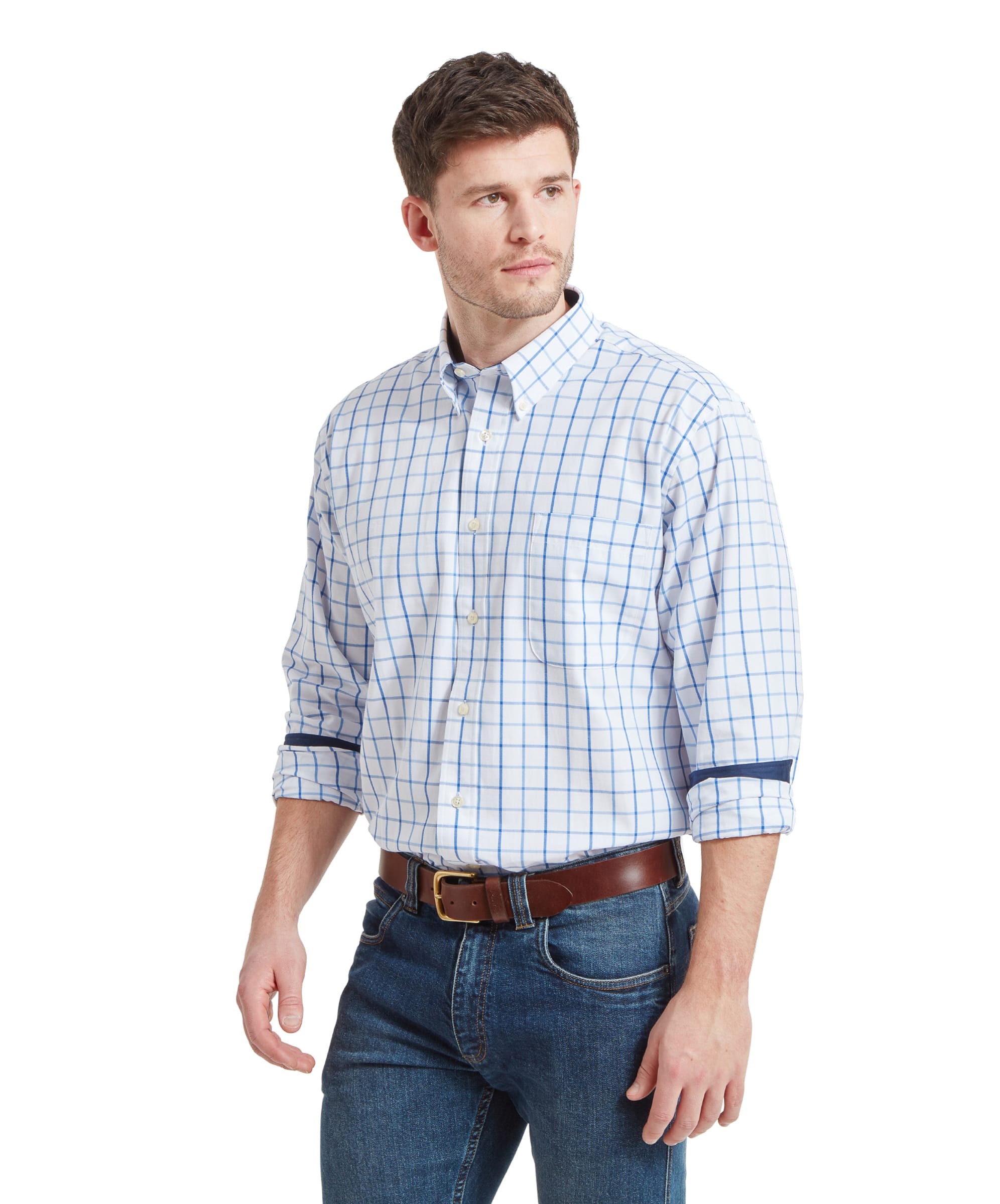 A man modeling a Schöffel Brancaster Classic Shirt for Men in Blue with long sleeves, paired with jeans and a brown belt. He has a neutral expression and is looking slightly to his left.