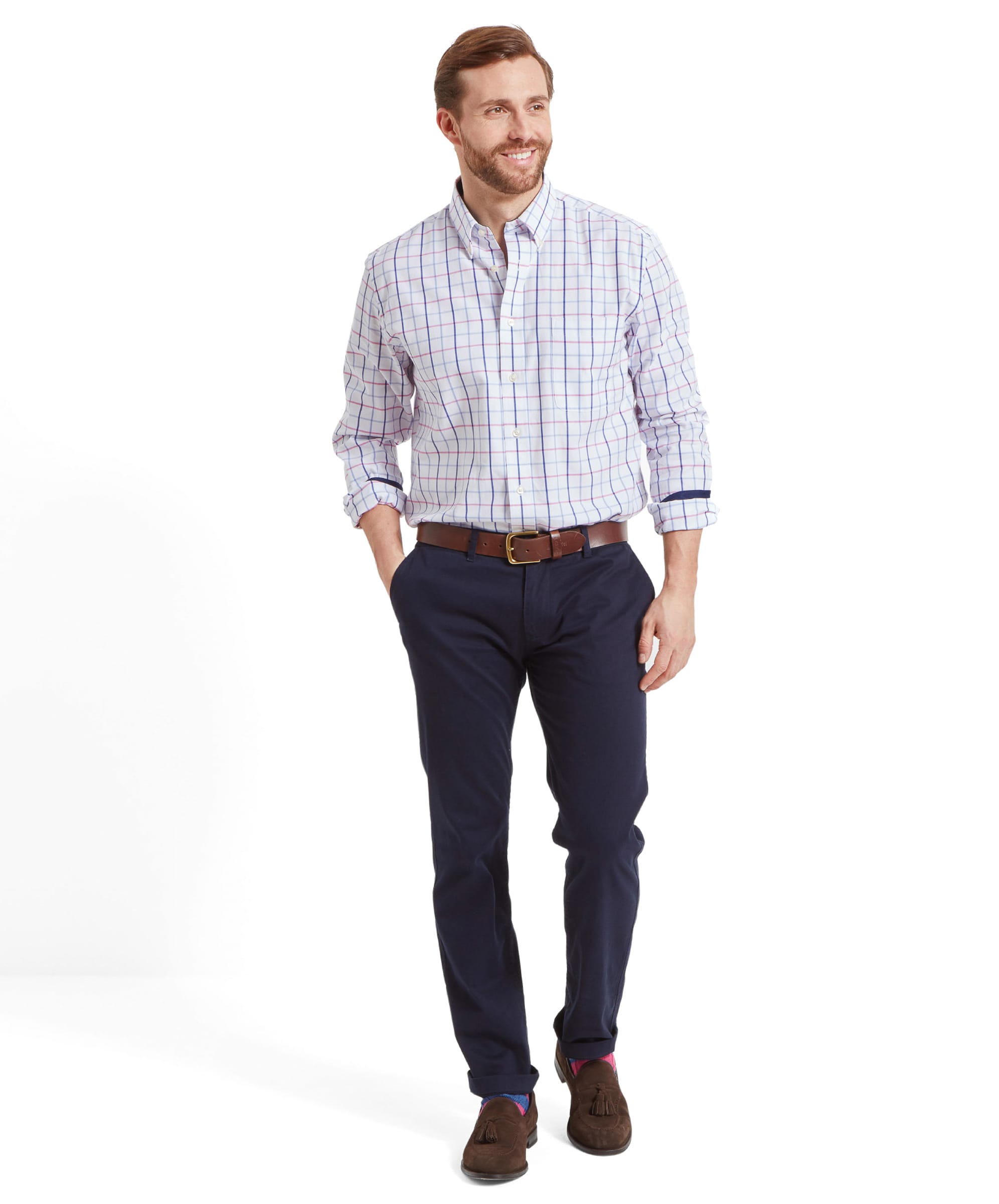 A full-body shot of a man wearing the Schöffel Brancaster Classic Shirt for Men in Pink, paired with dark blue trousers and brown shoes, standing and smiling with his hands in his pockets.