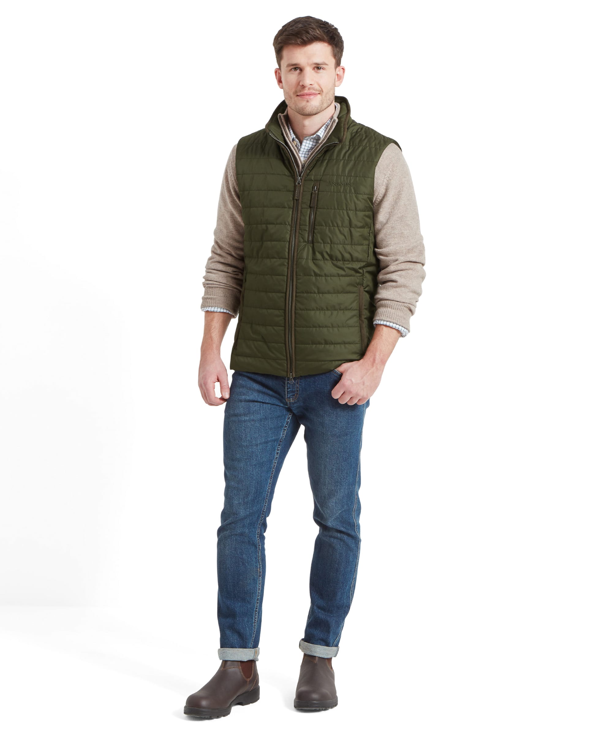 Full-body shot of the model wearing the Schöffel Brora Gilet for Men in Green, paired with a beige sweater, jeans, and brown boots.