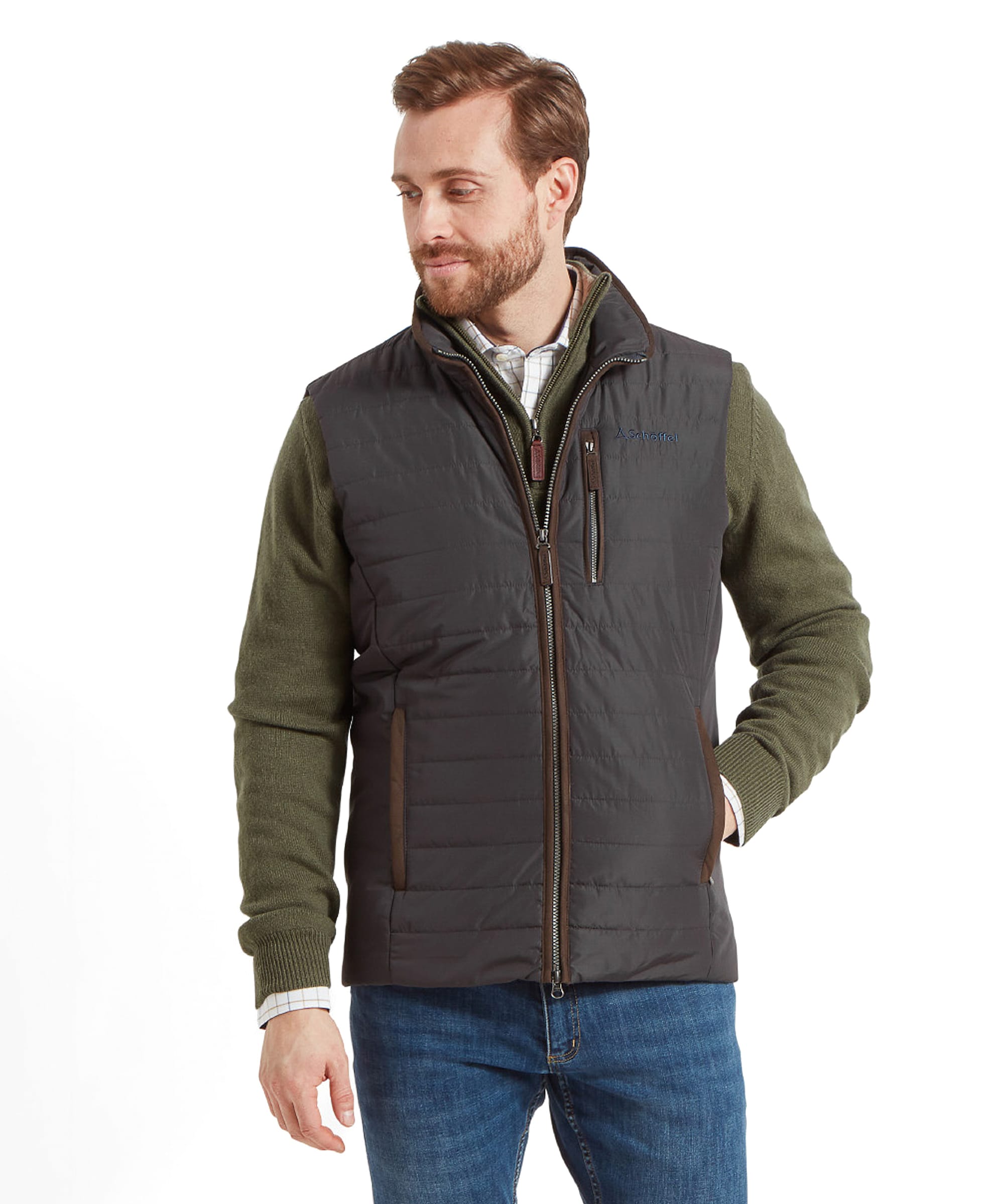 A man is seen wearing a Schöffel Brora Gilet for Men in Grey over a green sweater. The gilet is zippered and features a high collar, providing a stylish and warm look.