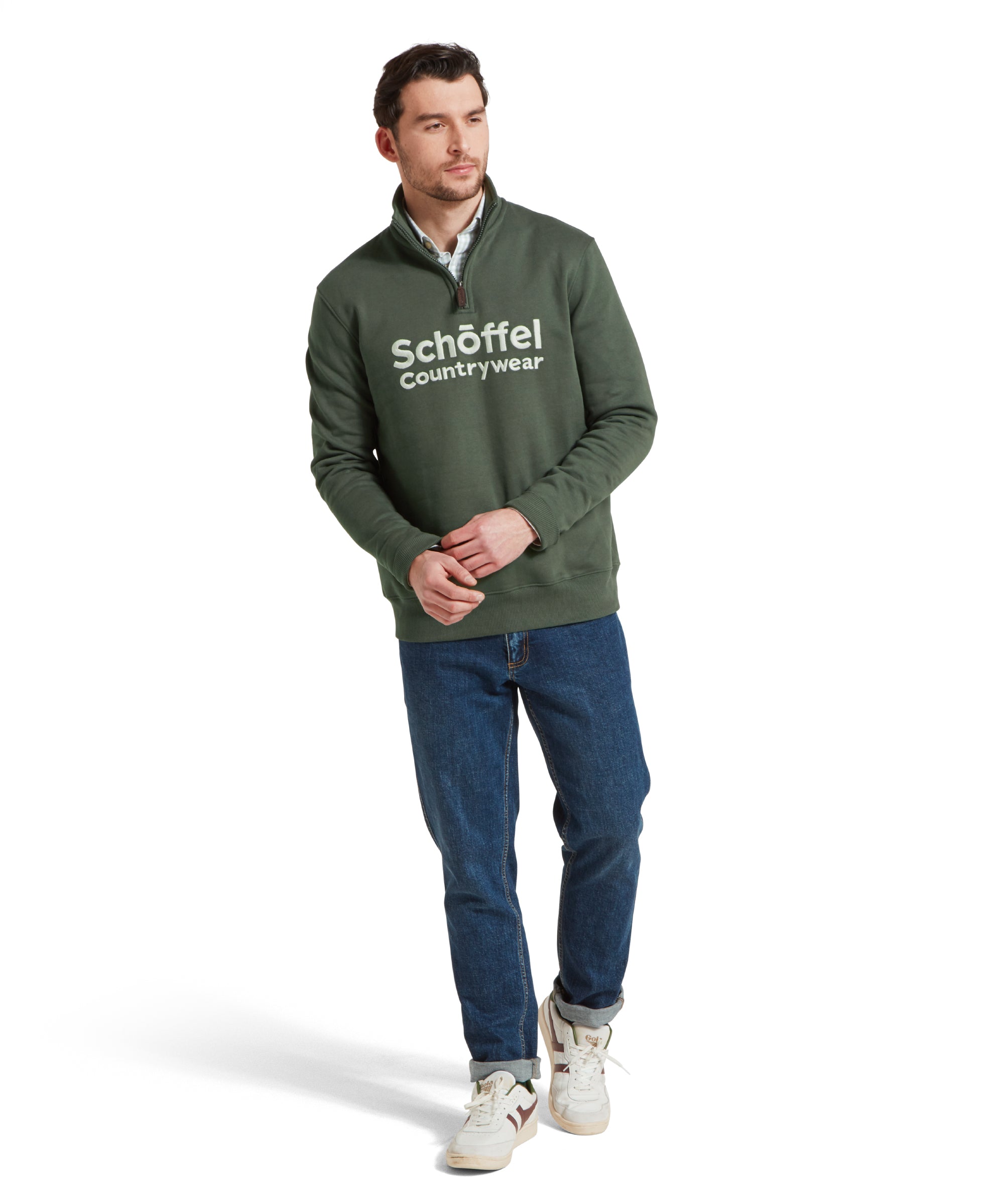 Full-body view of a man standing in a relaxed pose, wearing the Schöffel Bude Sweatshirt for Men in Green, paired with jeans and white trainers.