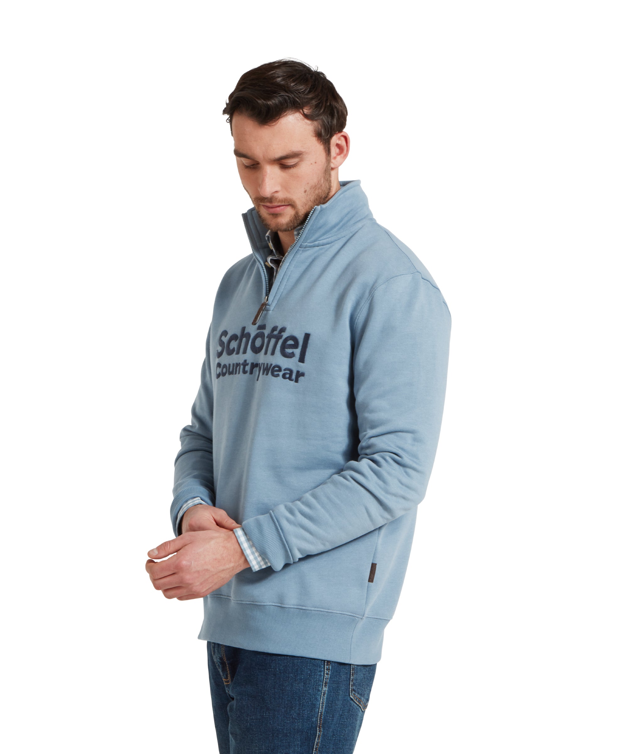 Side image of a man wearing the Schöffel Bude Sweatshirt for Men in Blue paired with dark blue jeans, navy trainers and checked shirt. He is standing in a relaxed pose looking down.