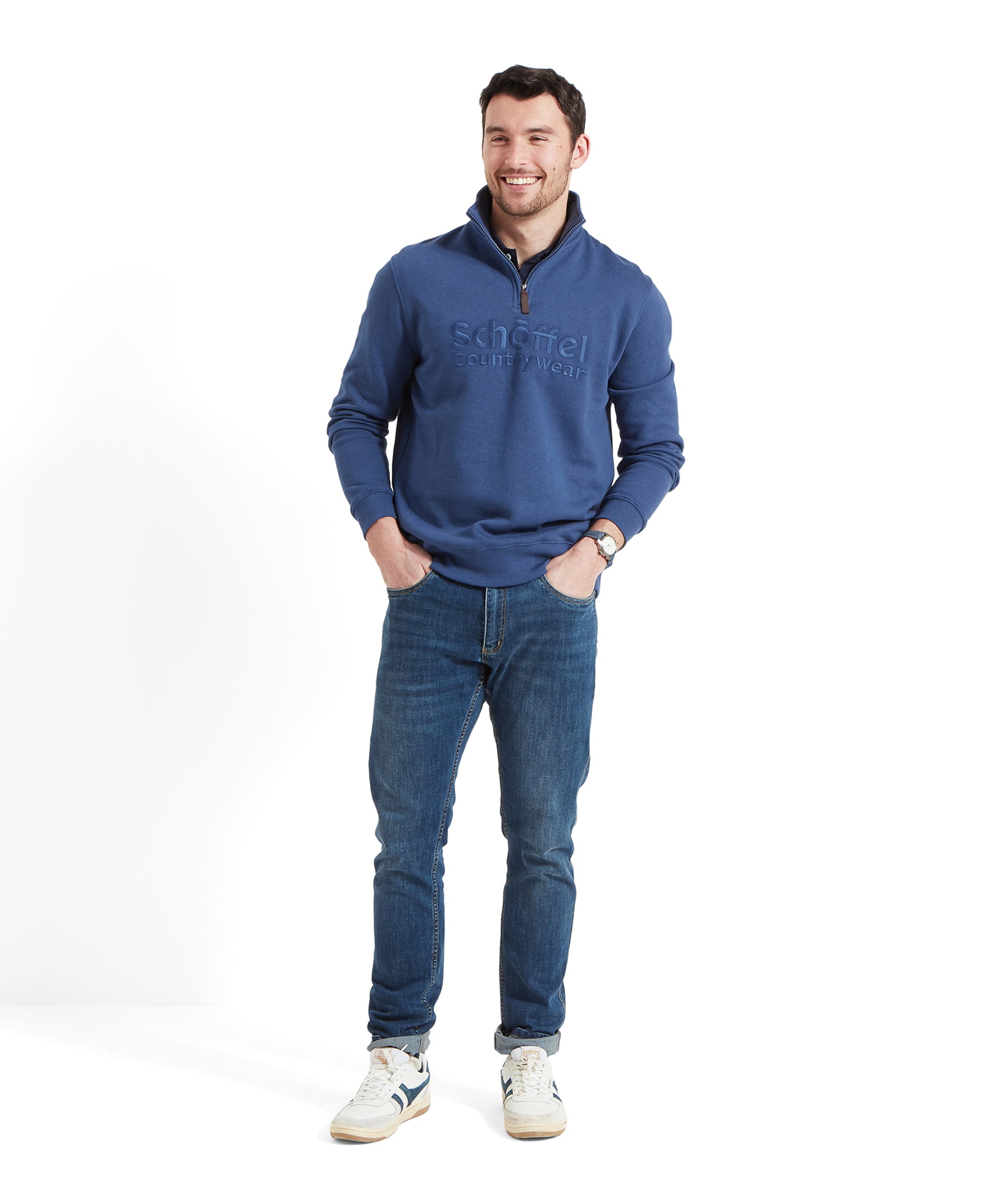 The same man in a Schöffel Bude Sweatshirt for Men in Blue, standing with his hands in his pockets, smiling and looking off to the side.