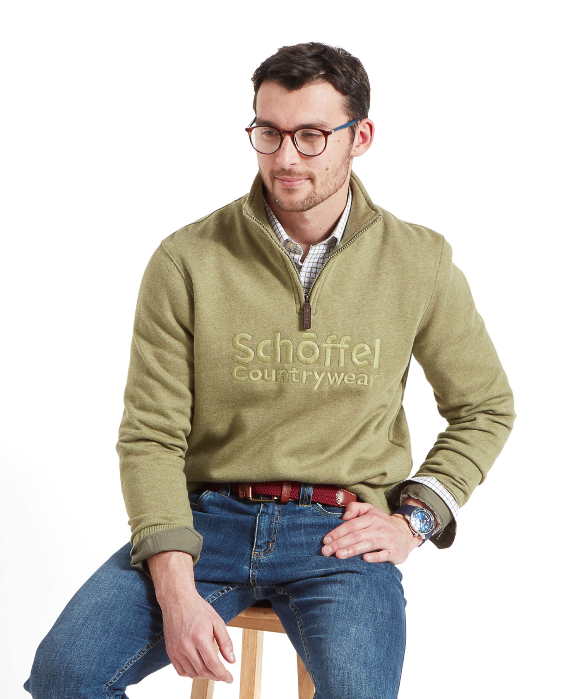 A man wearing the Schöffel Bude Sweatshirt for Men in Light Green, sitting on a stool and looking slightly to the side.