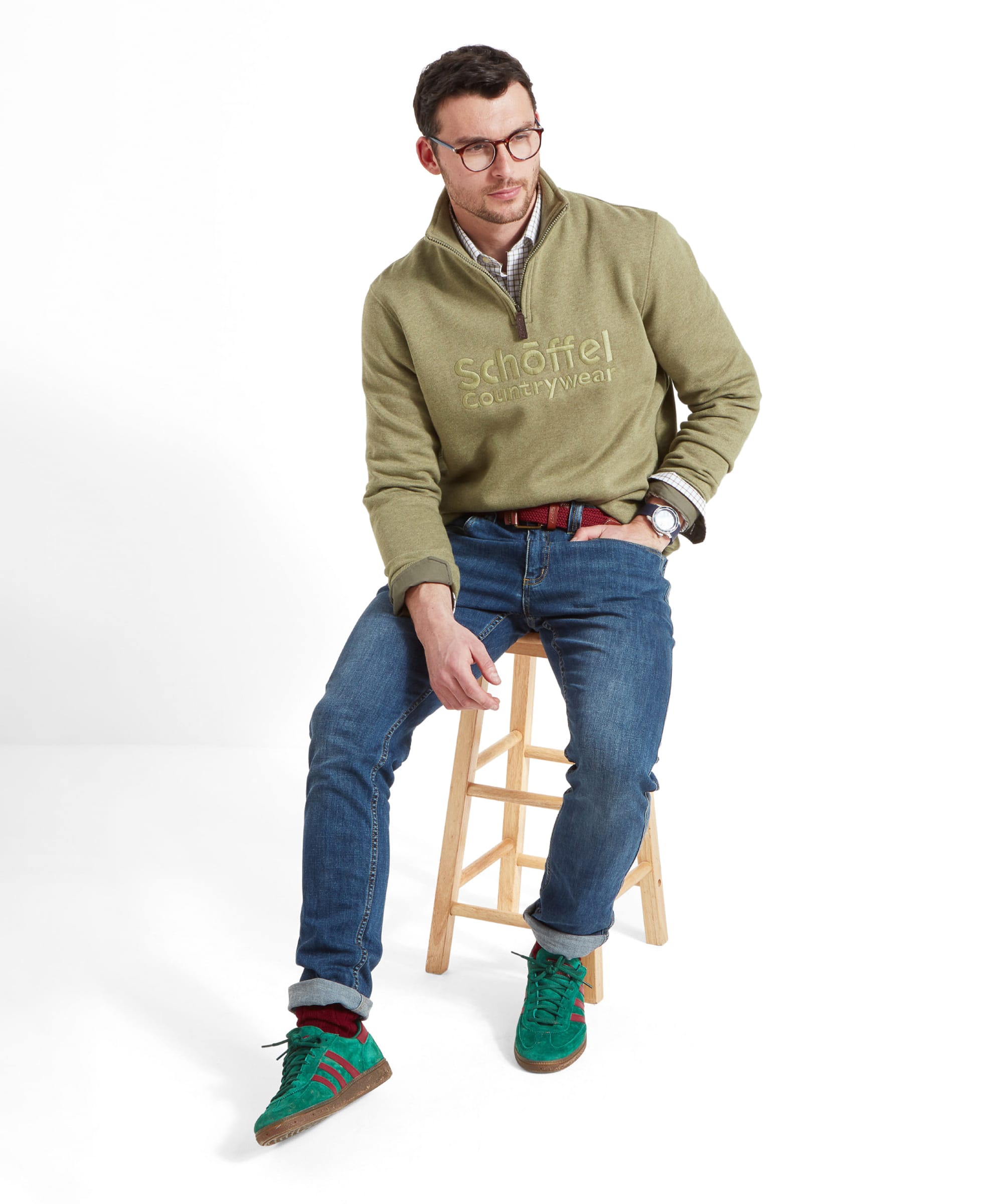 The man sitting on a stool, with the Schöffel Bude Sweatshirt for Men in Light Green clearly displaying the embroidered logo.