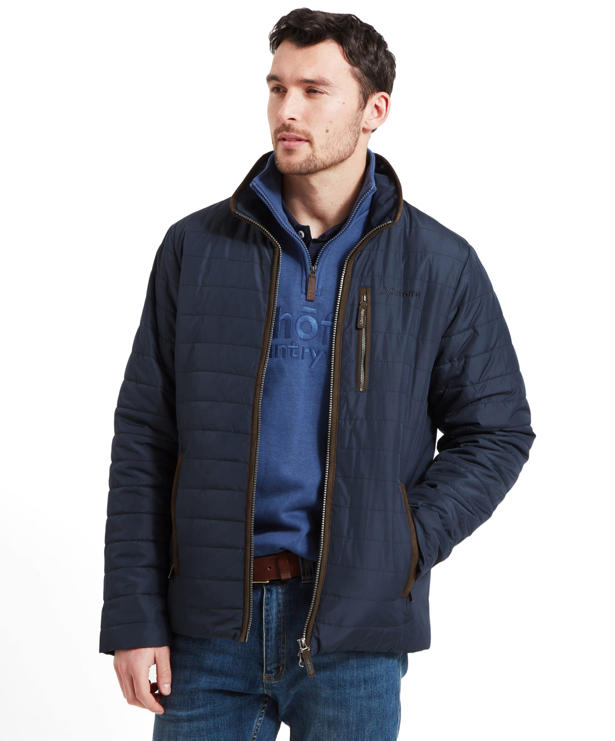 A man wearing the Schöffel Carron Jacket for Men in Navy, paired with a blue sweater, standing with his hands in his pockets.