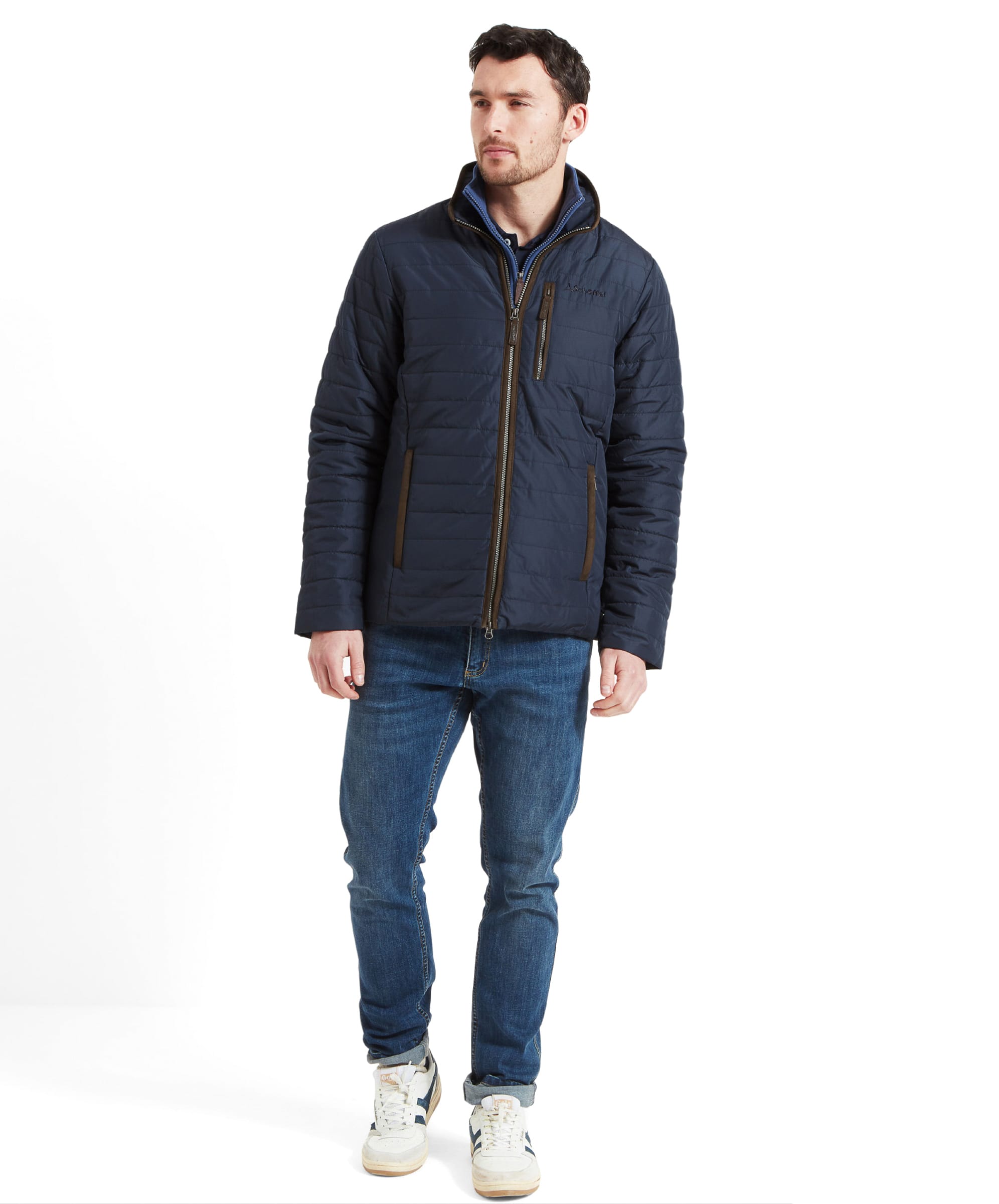 Full-body shot of the model in the Schöffel Carron Jacket for Men in Navy, showing the complete outfit with blue jeans and white trainers.