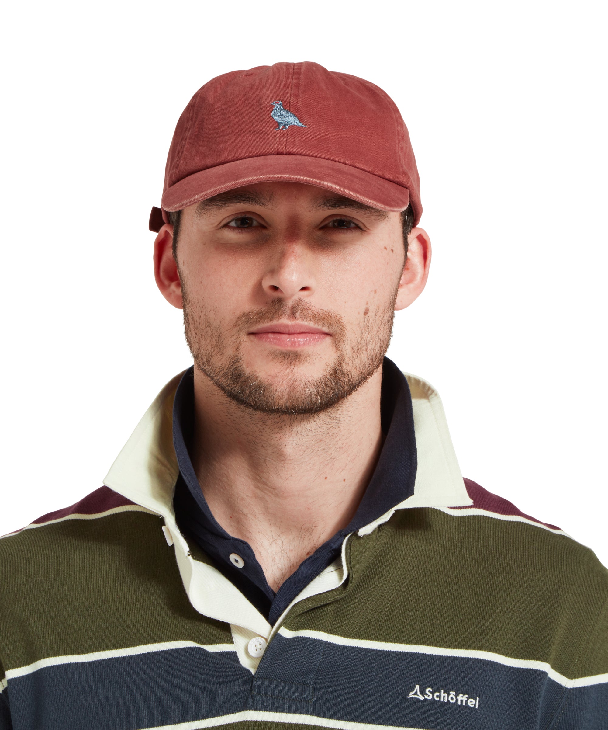 A close up of a male model wearing a red cap with blue embroidered bird logo on the front. It is paired with a green, blue and burgundy stiped rugby shirt and blue polo shirt.