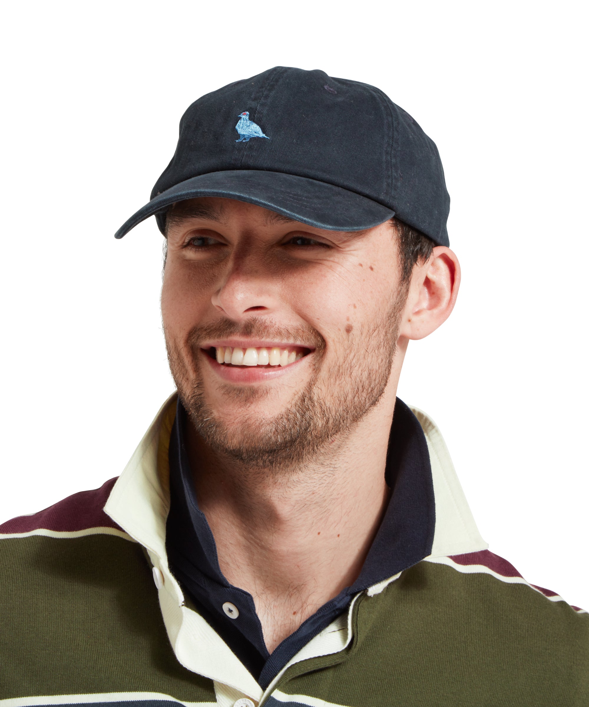 A close up of a male model wearing a navy cap with a light blue embroidered bird logo on the front. It is paired with a green, blue and burgundy stiped rugby shirt and blue polo shirt.