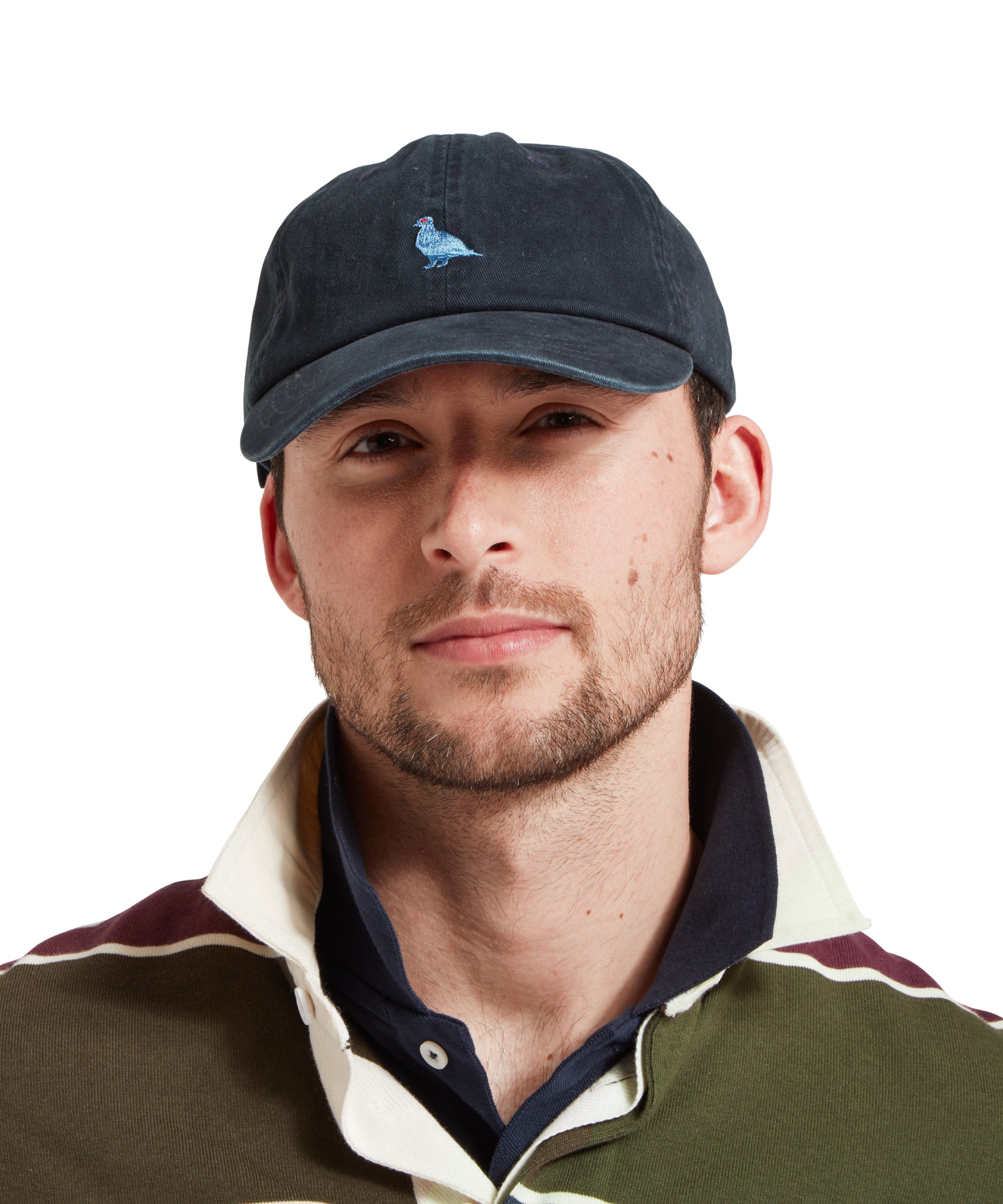 A close up of a male model wearing a navy cap with a light blue embroidered bird logo on the front. It is paired with a green, blue and burgundy stiped rugby shirt and blue polo shirt.