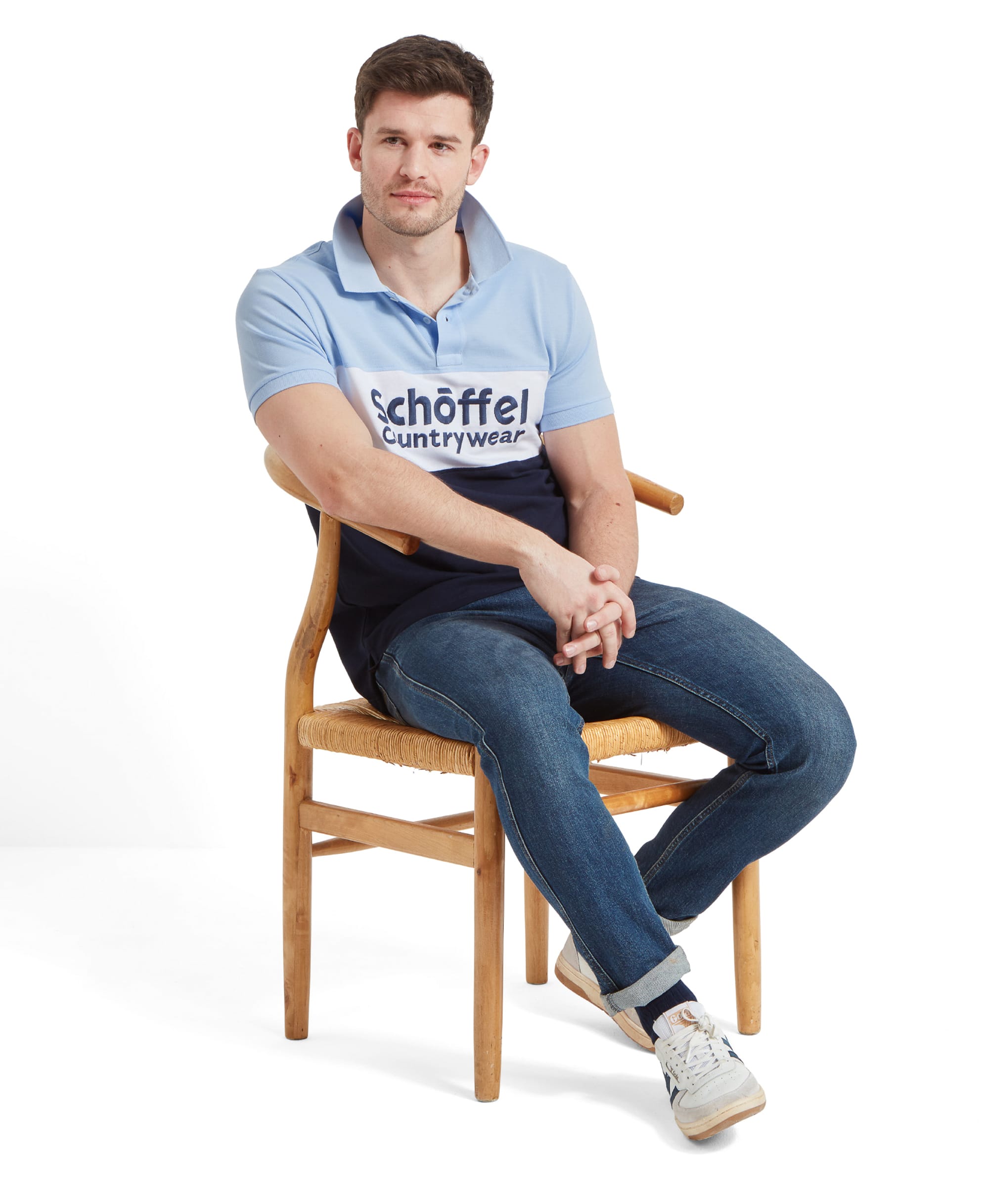 Full-body shot of the man sitting on the chair, showing the Schöffel Men's Exeter Heritage Polo Shirt in Blue and jeans.