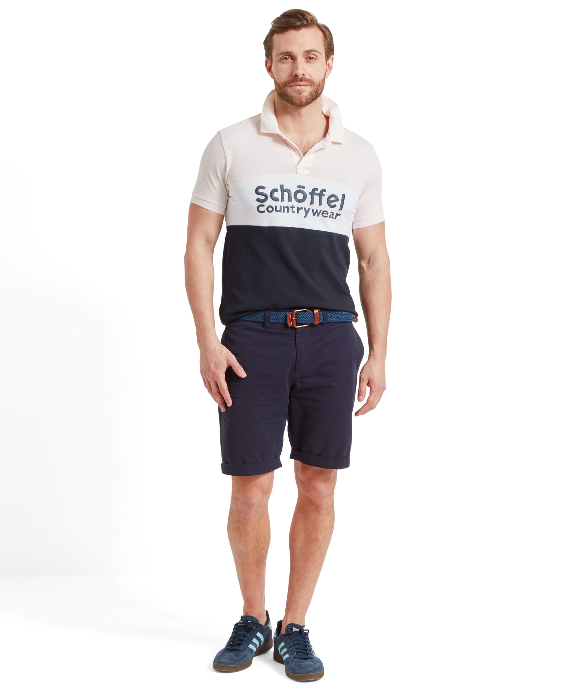 A full-body image of the man in a Schöffel Exeter Heritage Polo Shirt for Men in Pink, navy shorts, and blue sneakers, standing against a white background.