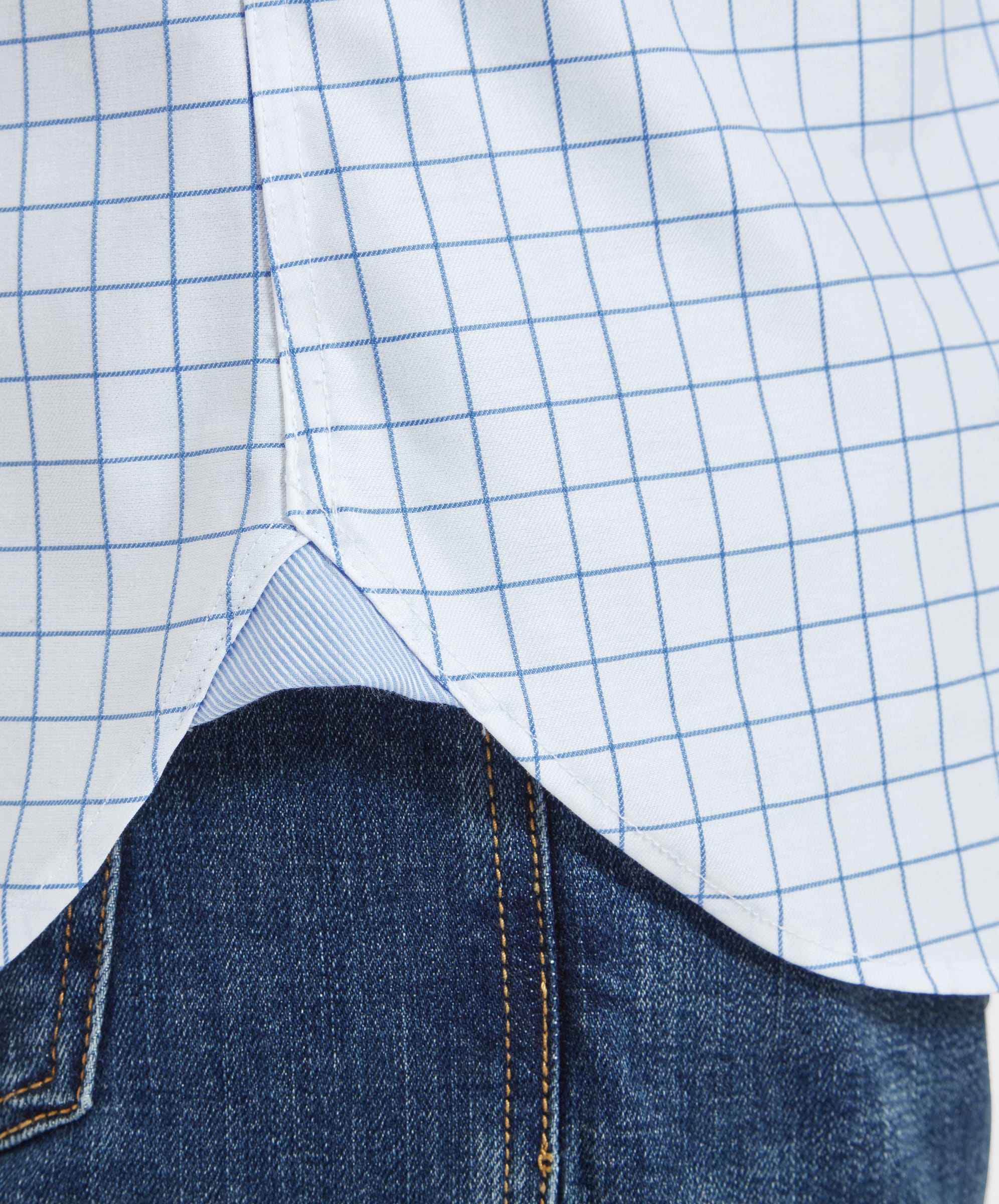 A close-up of the hem of the Schoffel Greenwich Tailored Shirt for Men in Blue Check, showing the gusset detail and the shirt's fabric against the man's blue jeans.