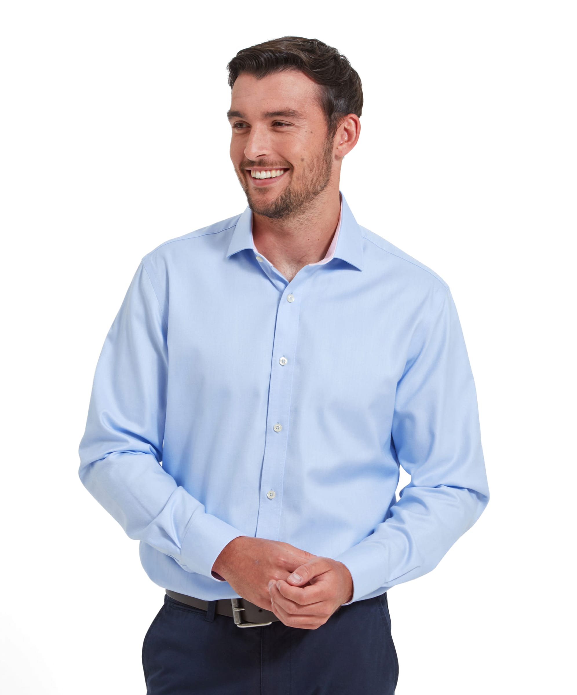 A man wearing a Schöffel Greenwich Tailored Shirt for Men in Blue. The shirt is paired with navy trousers and a black belt. He is standing with his hands clasped in front and smiling.