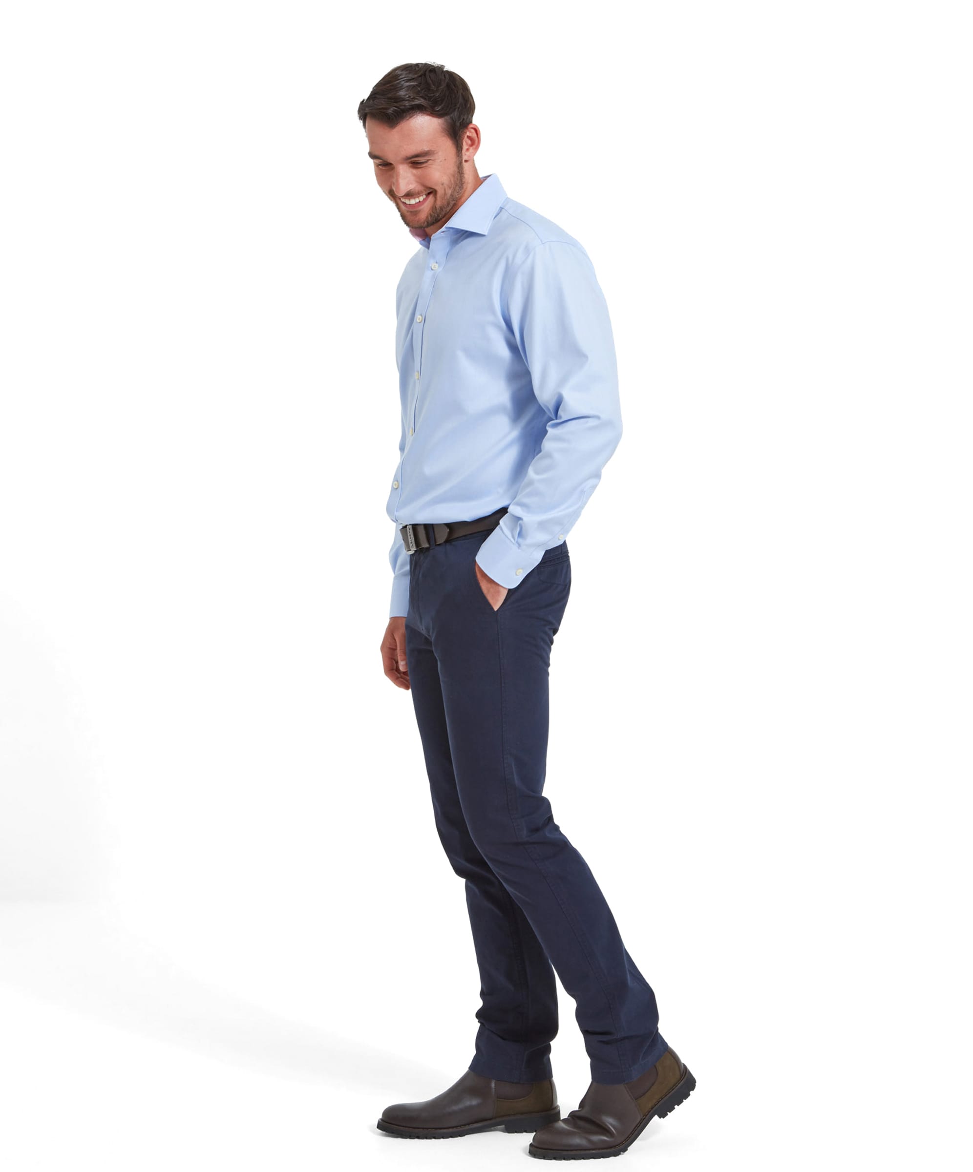 A full-body side view of the same man wearing the Schöffel Greenwich Tailored Shirt for Men in Blue, smiling and looking downwards, showing the shirt and trousers' fit.