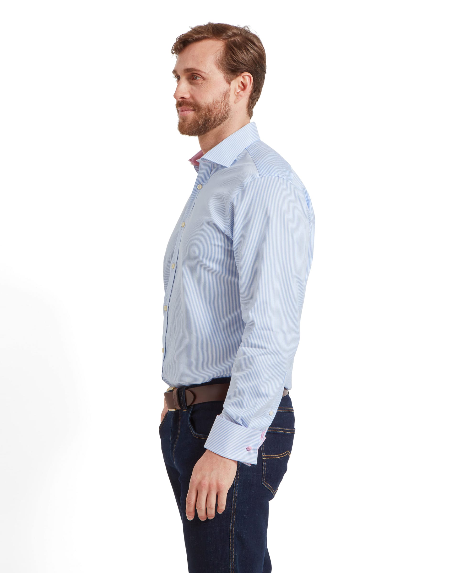 A side profile of a man wearing a Schöffel Greenwich Tailored Shirt for Men in Blue Stripe, looking forward. He is also wearing dark blue jeans and a brown belt.