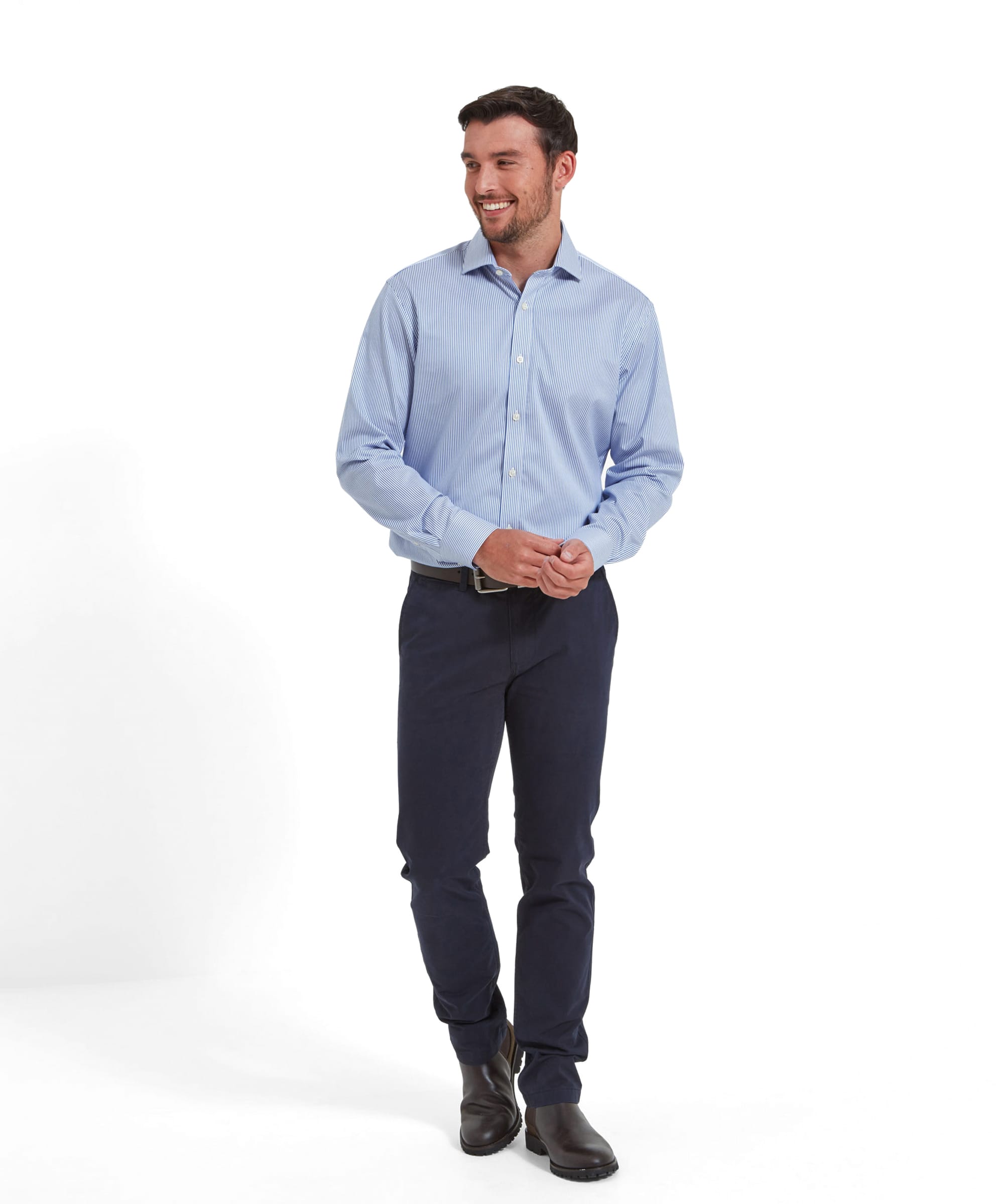 The same man in the Schöffel Greenwich Tailored Shirt for Men in Navy Stripe, standing and smiling, with hands clasped. He is wearing navy trousers and brown shoes, showcasing the shirt's professional and polished look.