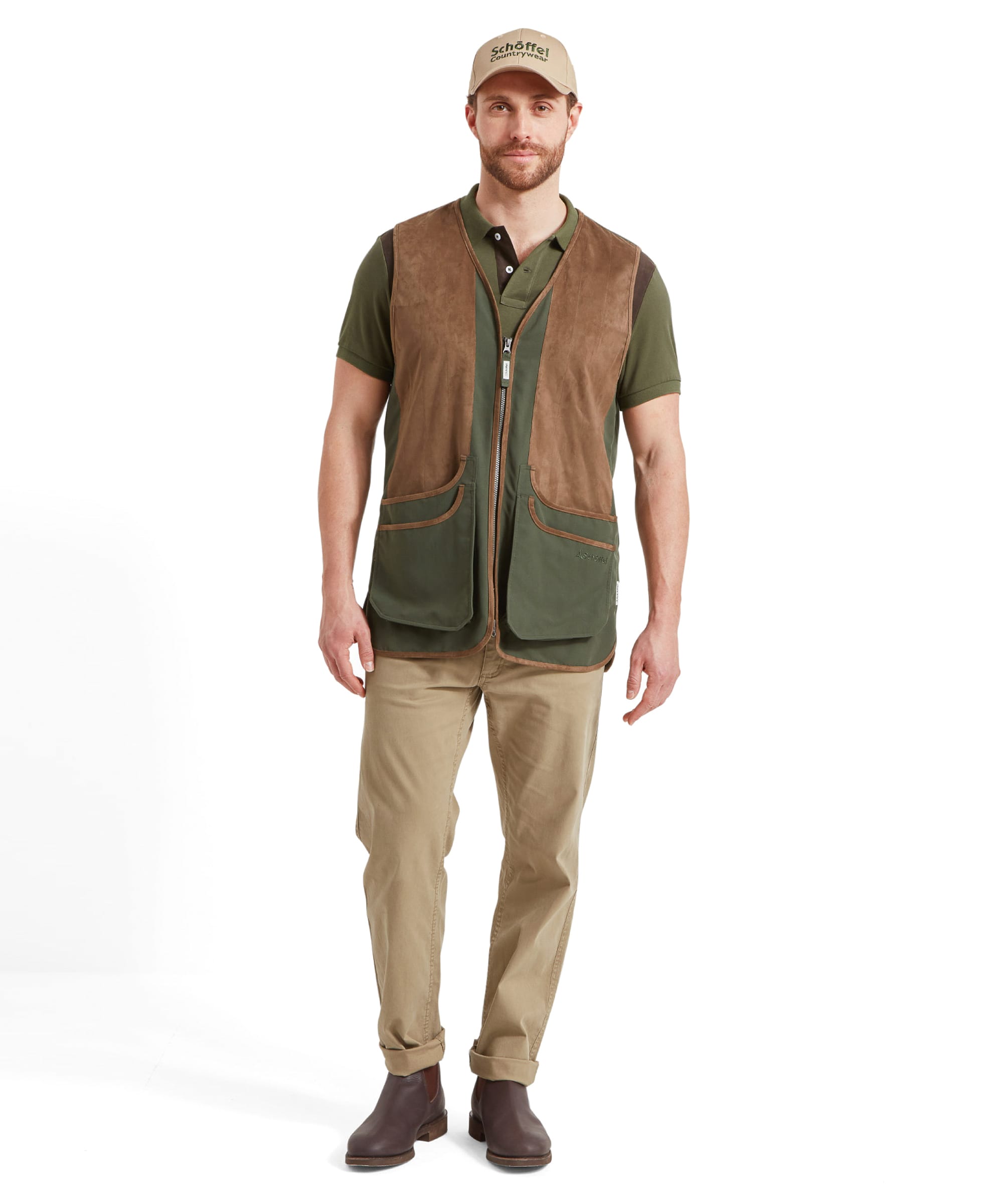 Full-body view of a man wearing the Schöffel Grimsthorpe Clay Shooting Vest for Men in Green, paired with beige trousers and brown boots. Model is looking forward and wears a beige cap.