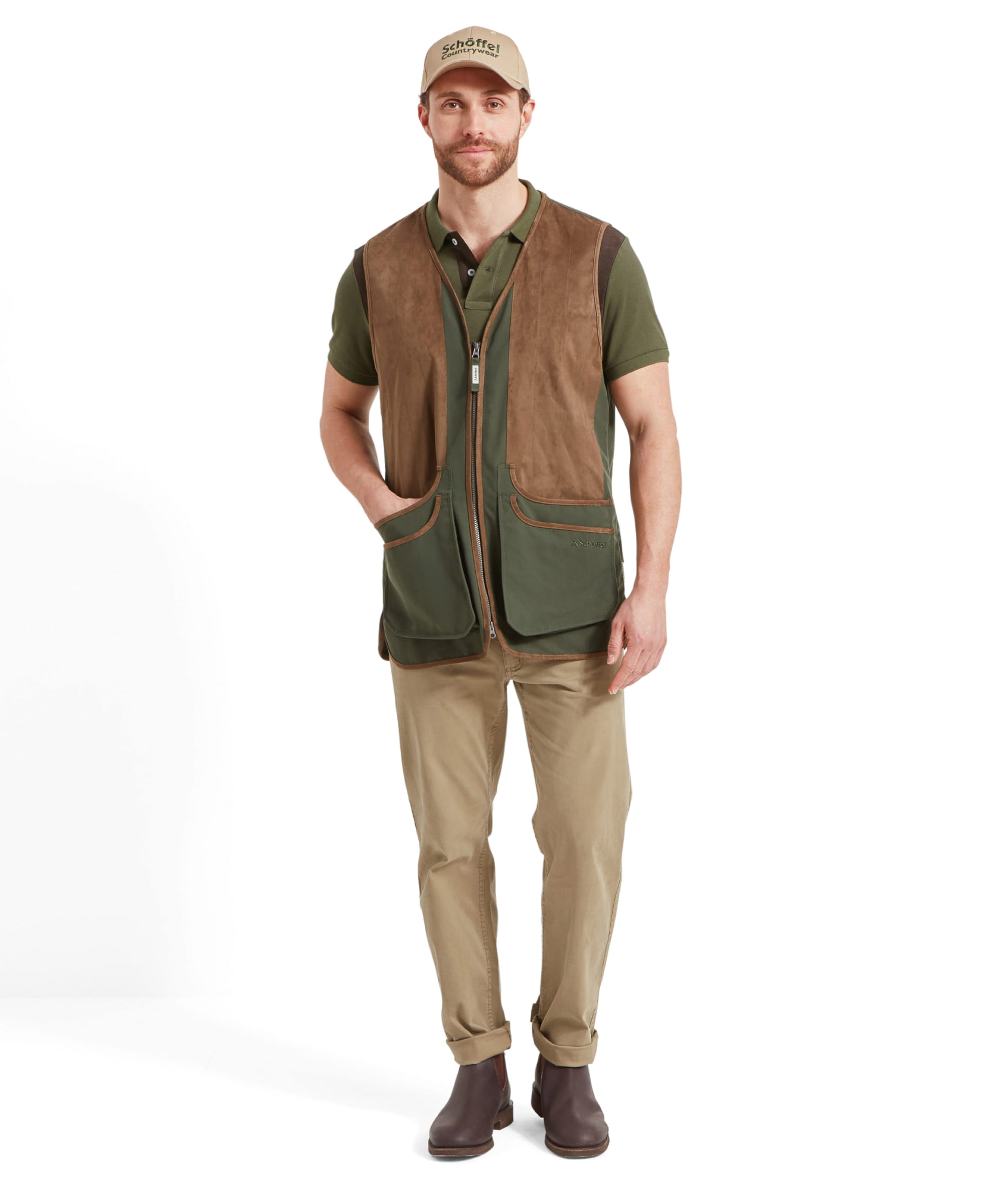 Full-body view of a man wearing the Schöffel Grimsthorpe Clay Shooting Vest for Men in Green with his left hand in the pocket, paired with beige trousers and brown boots. Model is looking forward and wears a beige cap.