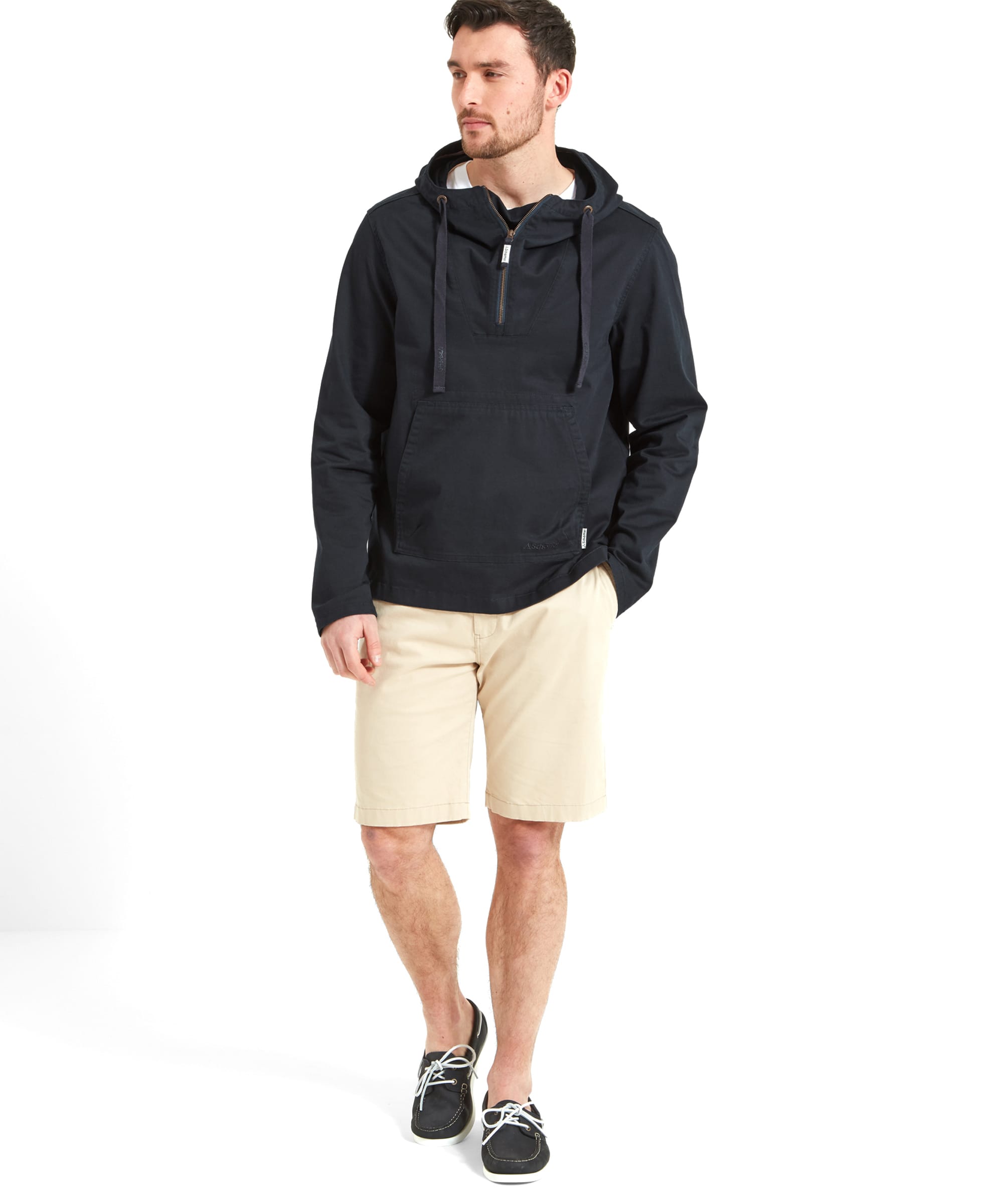 A full-body view of the model wearing the Schöffel Harbour Smock for Men in Navy with beige cream shorts and navy deck shoes. The model has his right hand in the shorts pocket and he's looking to his left