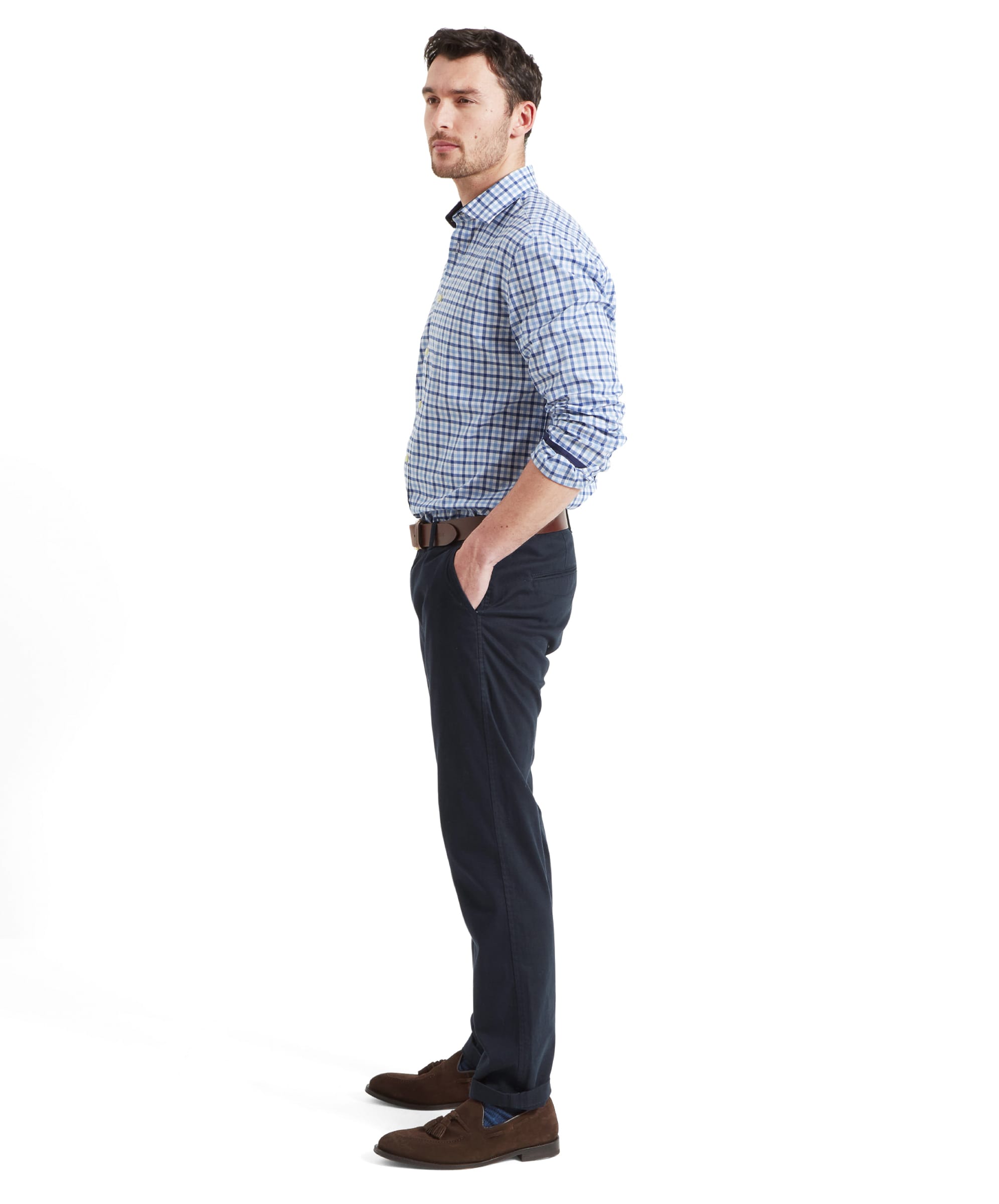 Full body side view of a man wearing the Schöffel Hebden Tailored Shirt for Men in Blue Navy with blue trousers, a brown leather belt and brown suede loafers. He has his hands in the trouser pockets and the short sleeves are rolled up his forearms.