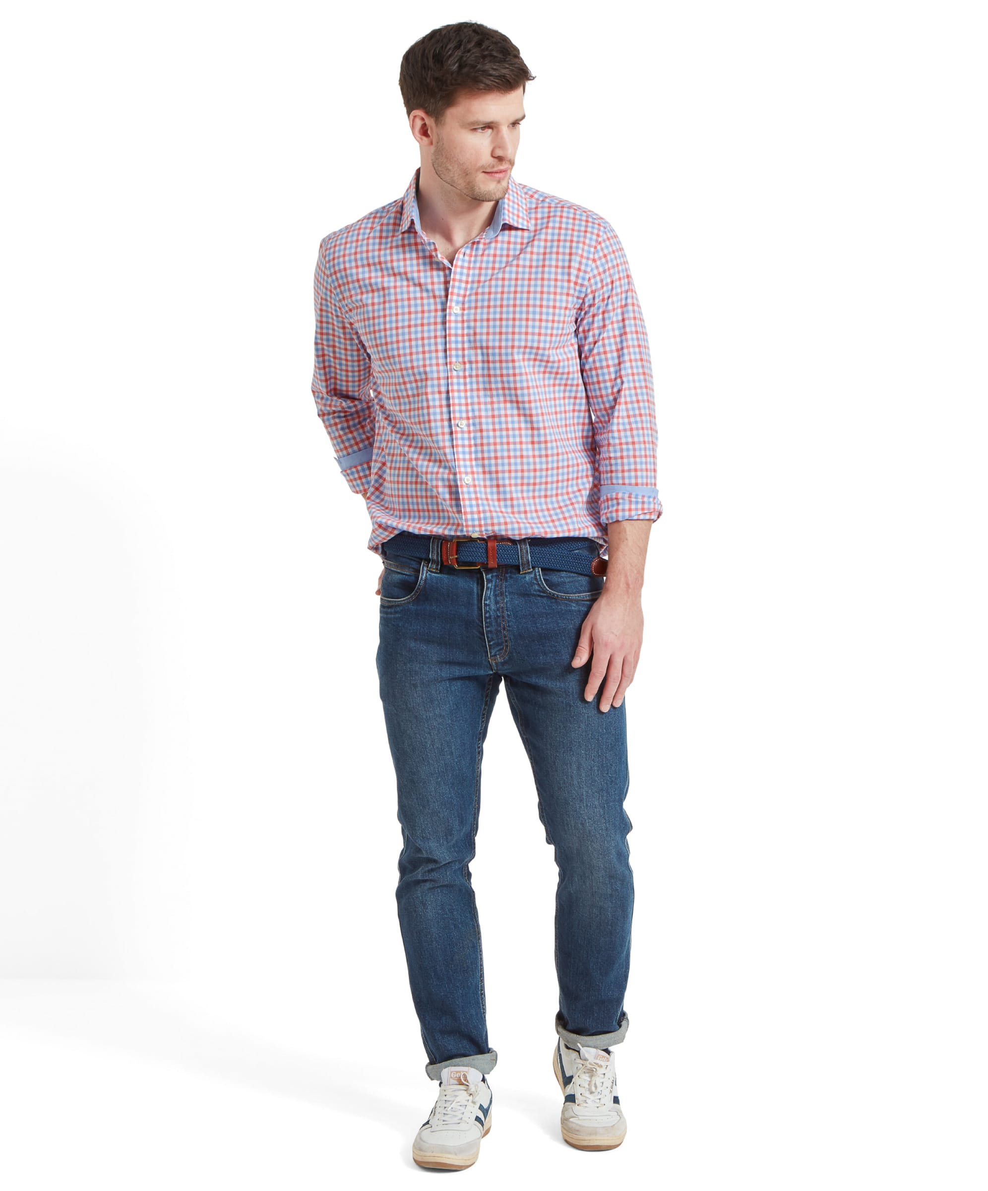 Full body shot of a man wearing the Schöffel Hebden Tailored Shirt for Men in Coral and Blue partnered with blue jeans, blue woven belt and white trainers. The mans sleeves are rolled up his forearms and he has his right hand in his back jean pocket.