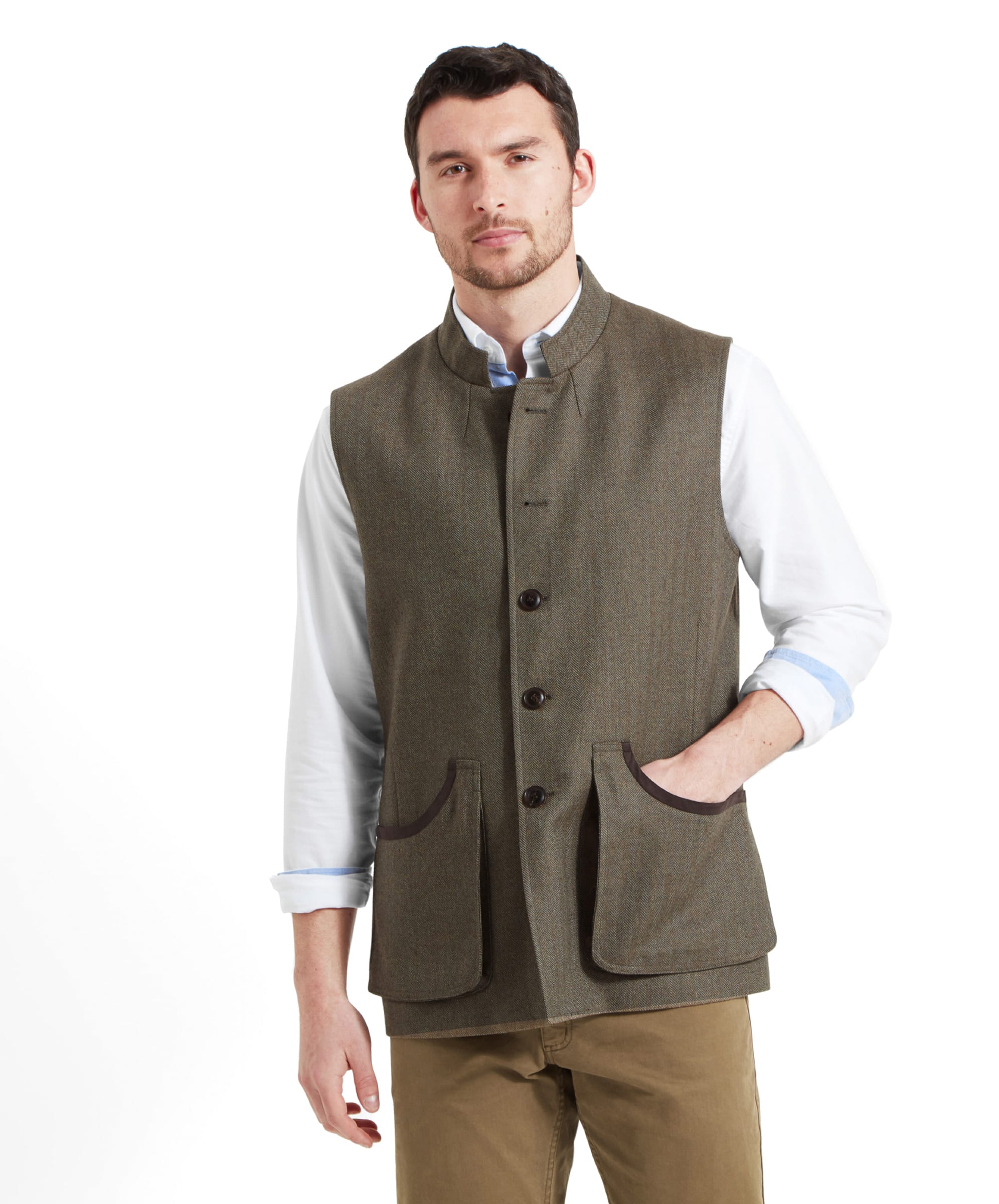 A man wears the Schöffel Holcot Tweed Waistcoat for Men in Green with a white shirt and tan trousers. He has his right hand in the waistcoat pocket which is a deep billow design with a brown edge trim.