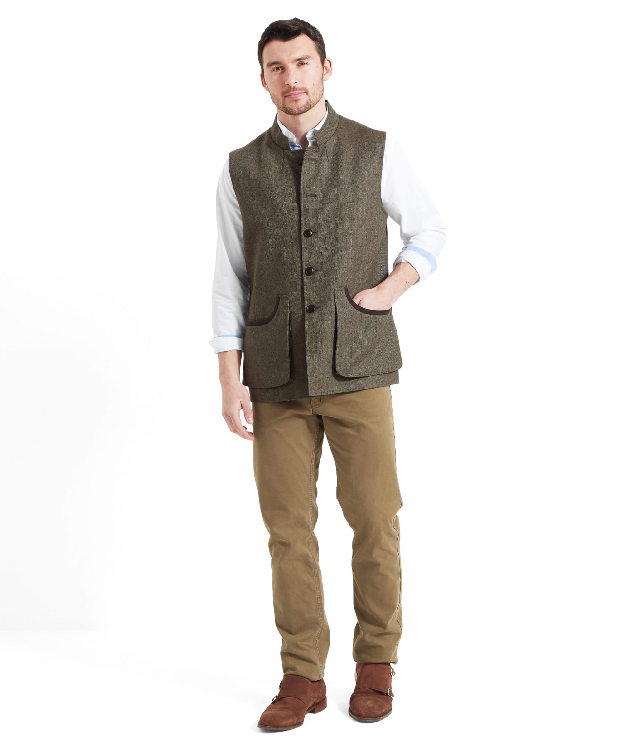 Full body view of a man wearing the Schöffel Holcot Tweed Waistcoat for Men in Green with a white shirt, tan trousers and brown suede shoes. He's walking forward with his right hand in the waistcoat pocket.