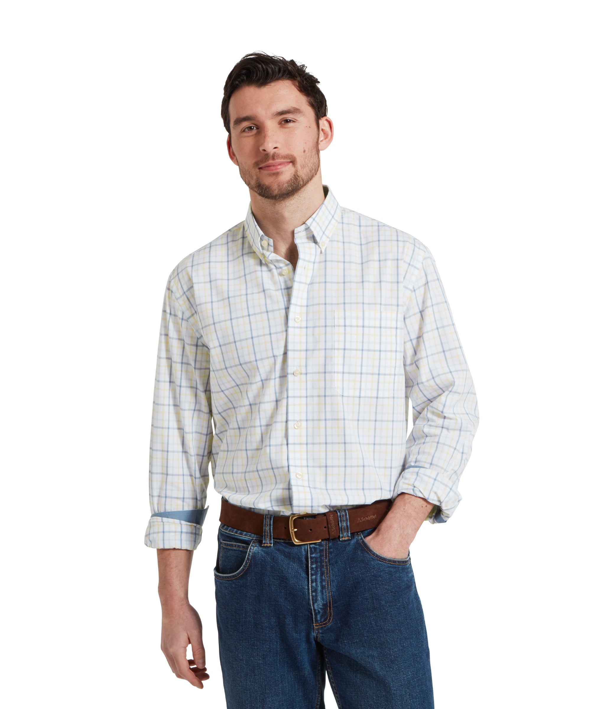 A man wears the Schöffel Holkham Classic Shirt for Men in Blue with the collar open and the sleeves rolled up slightly. He has partnered with dark navy jeans and a brown leather belt. He has his left hand placed in his jeans pocket.